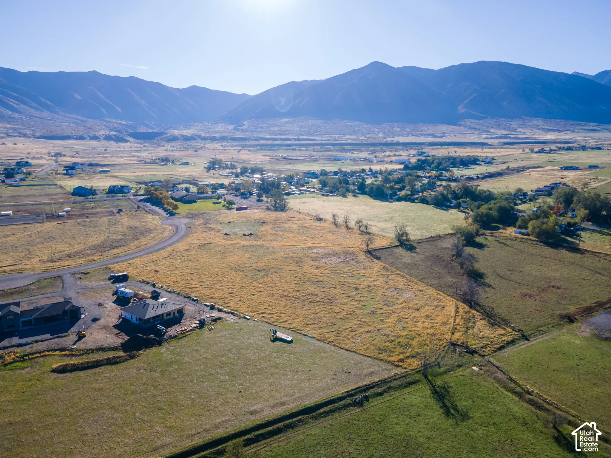 Aerial perspective of expansive acreage featuring paved road frontage, natural topography, and a prominent mountain range backdrop
