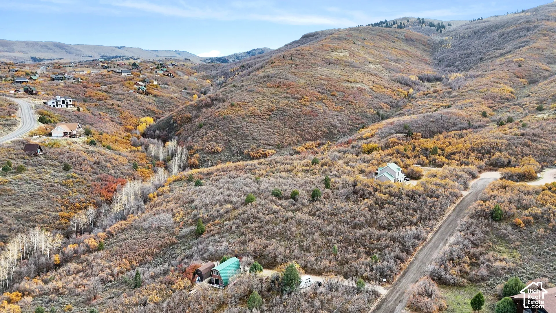 Aerial perspective of mountainous terrain featuring native scrub oak, scattered evergreen trees, winding gravel access roads, and natural slope topography