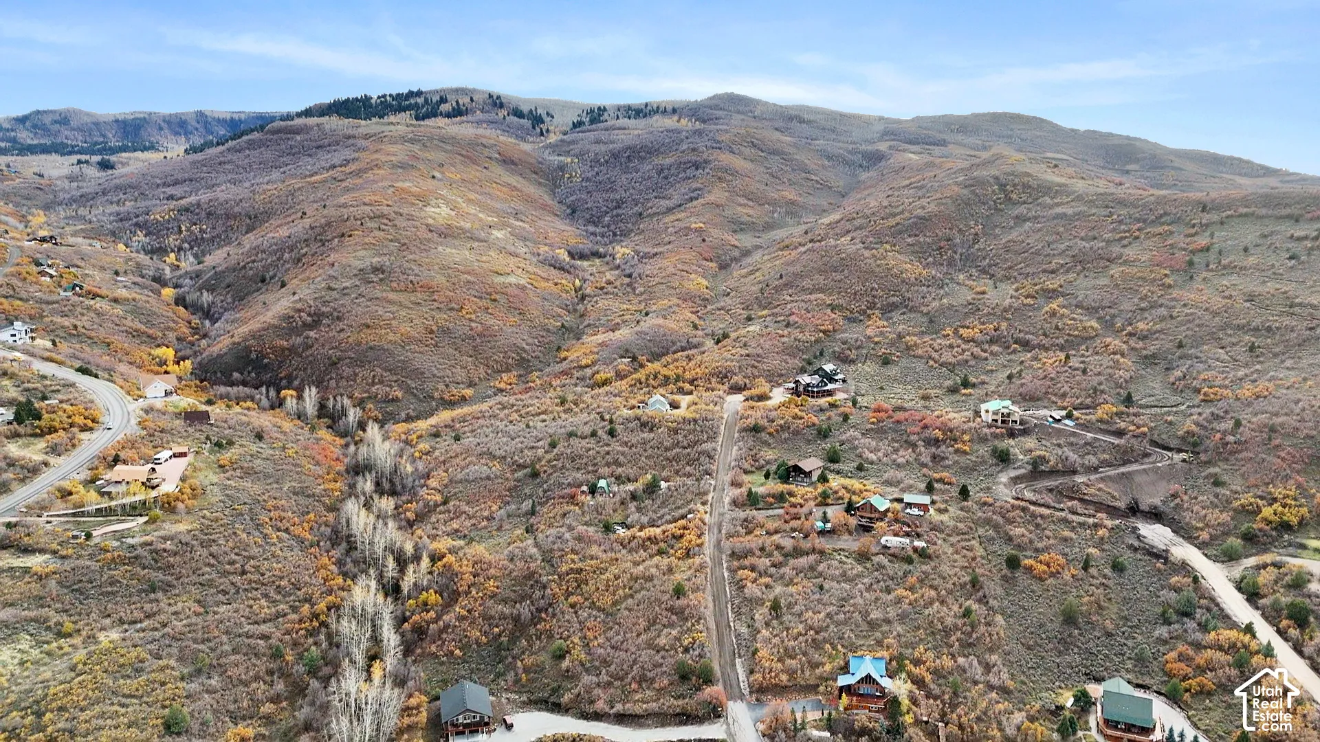 Aerial perspective of mountainous terrain featuring expansive hillside topography, deciduous vegetation, and winding access roads