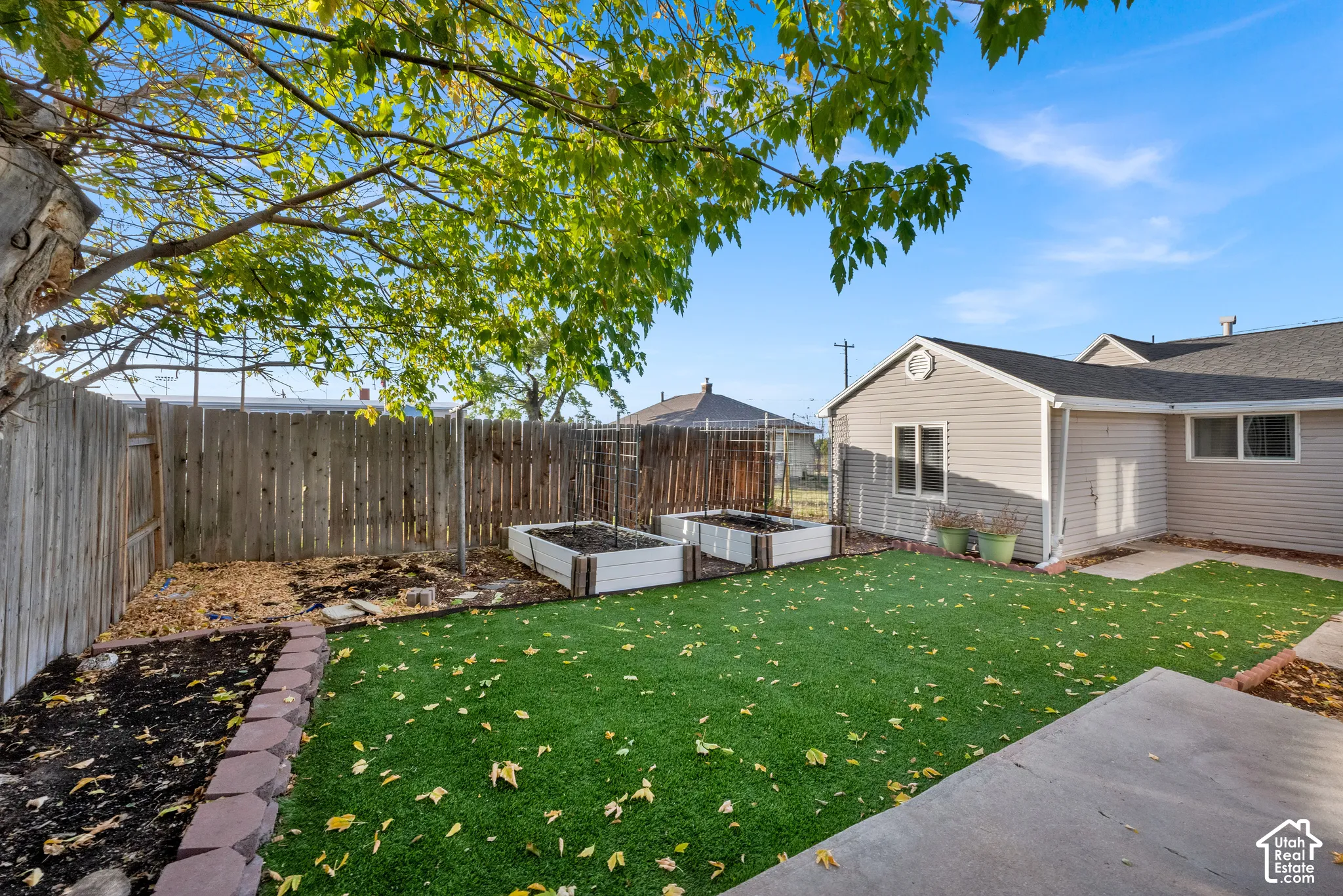 Rear exterior featuring synthetic turf lawn, raised garden beds, concrete patio, and wood privacy fencing