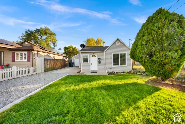Exterior featuring grey horizontal siding, a gravel driveway, a detached garage, and a landscaped front lawn