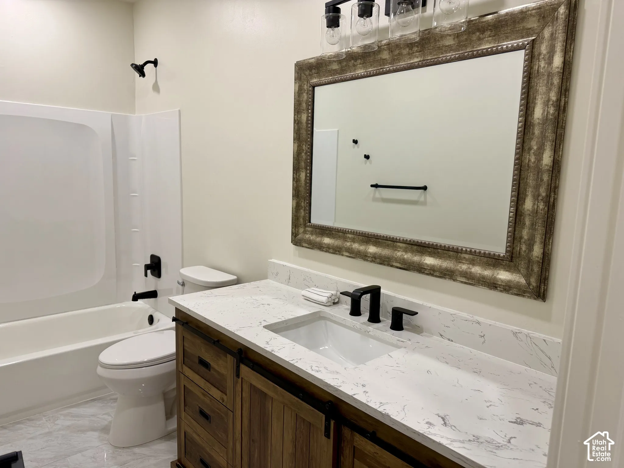 Bathroom vanity featuring a stone-look countertop, integrated rectangular sink, wood-finish cabinetry with sliding hardware, matte black faucet, and matching multi-light fixture above a framed mirror