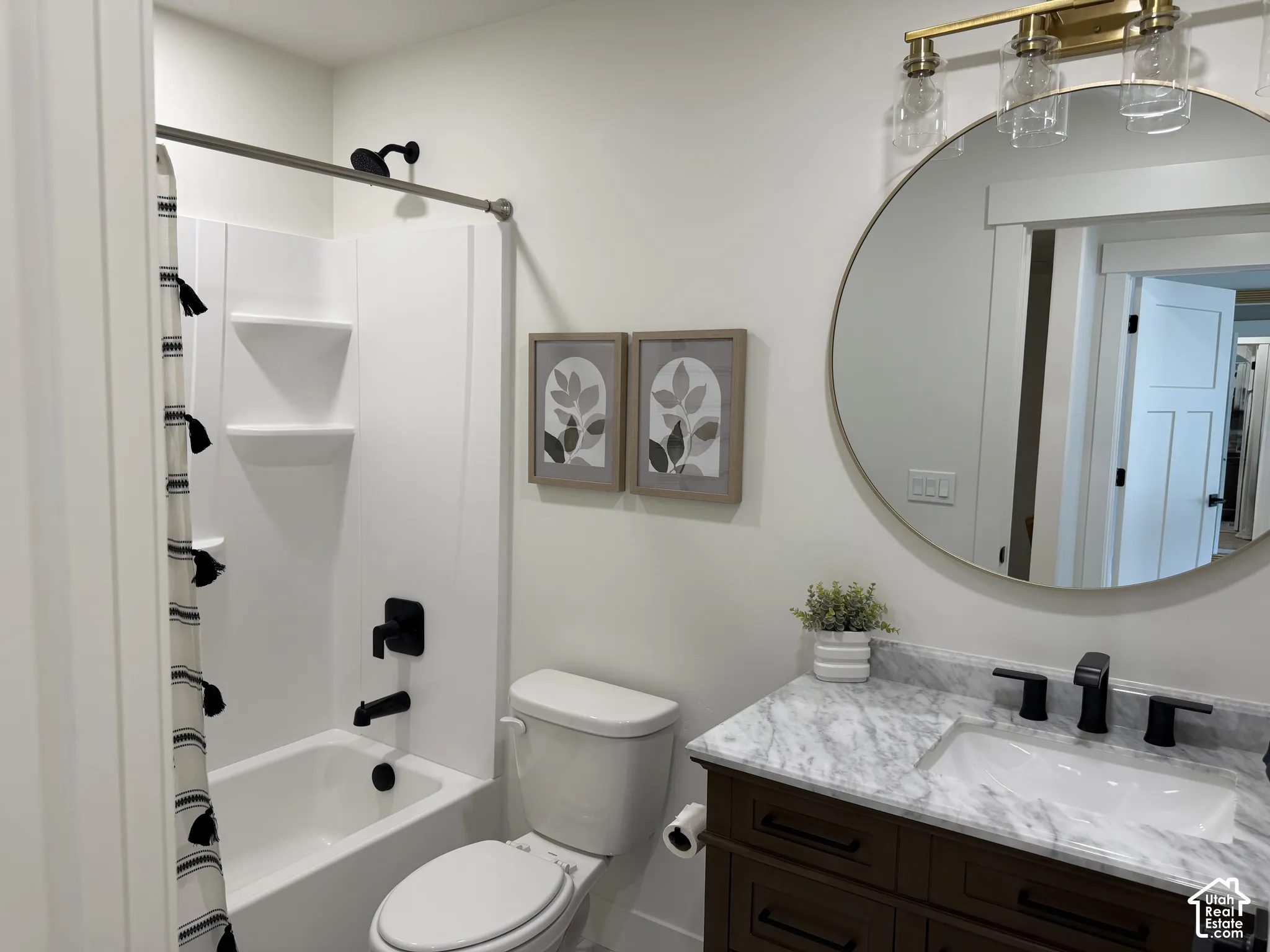 Bathroom featuring a dark wood vanity with a stone countertop, an undermount sink with matte black hardware, a circular mirror with a metallic frame, and a tub-shower combination with built-in shelving