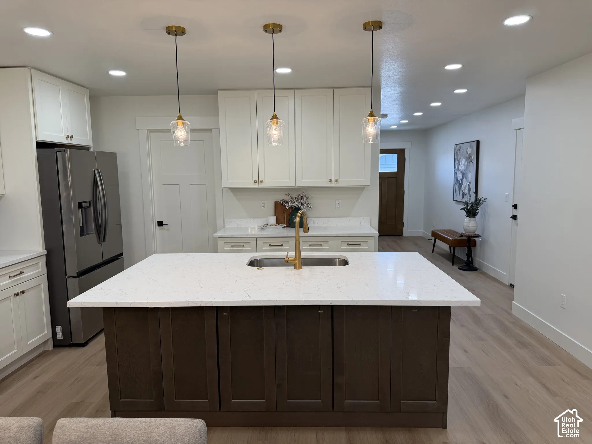 Kitchen island featuring a stone-look countertop, undermount sink with a brass-finish faucet, and custom cabinetry