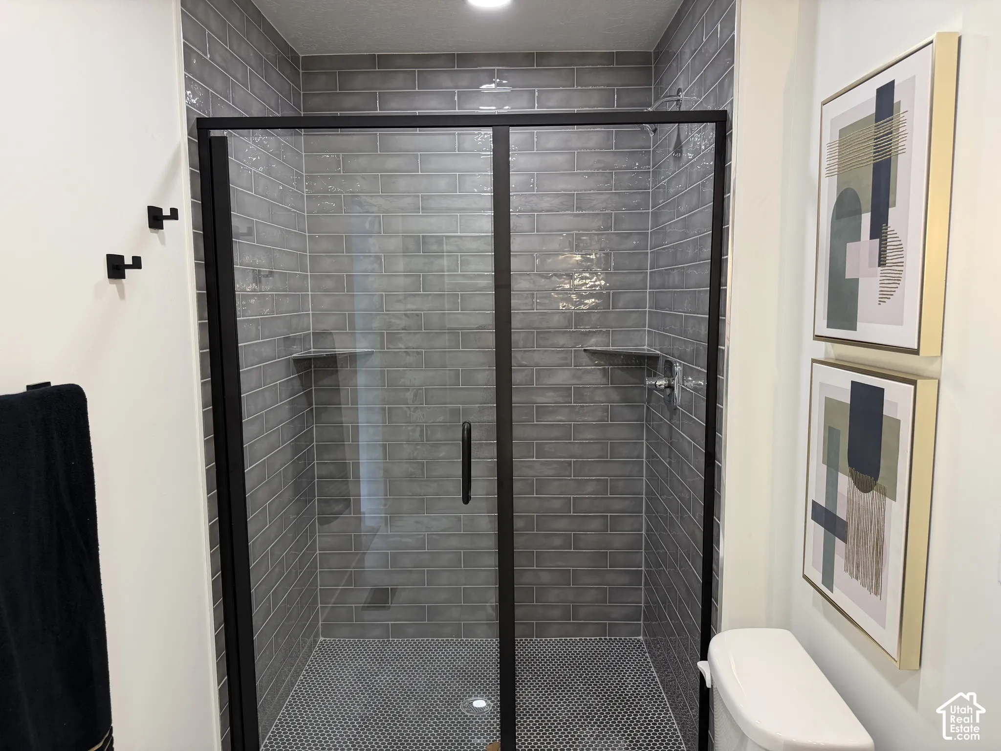 Walk-in shower featuring grey subway-style wall tile, mosaic floor tile, a matte black framed glass door, and built-in corner shelving