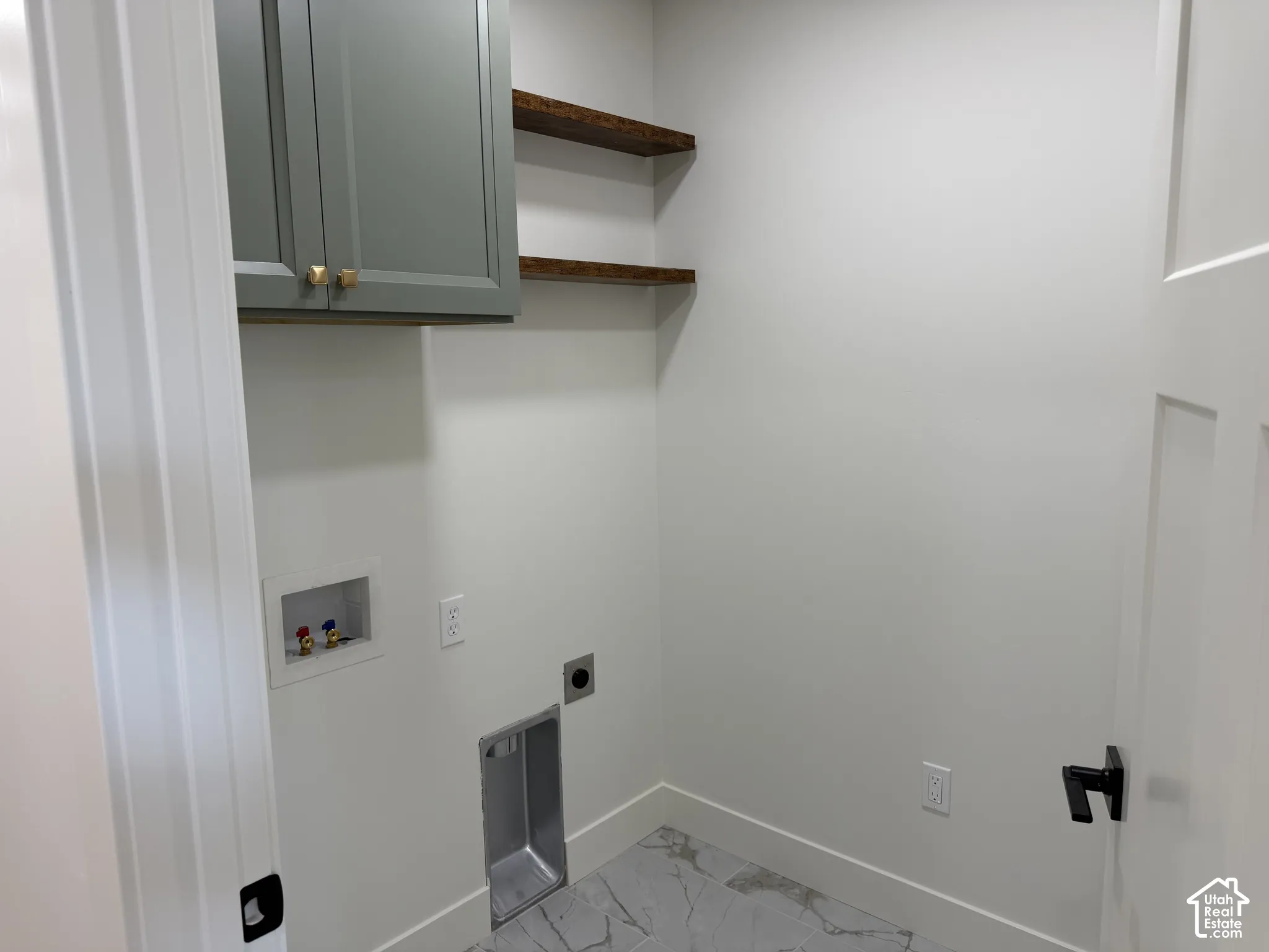 Laundry area featuring grey shaker-style wall cabinetry, wood-finish open shelving, and stone-patterned tile flooring