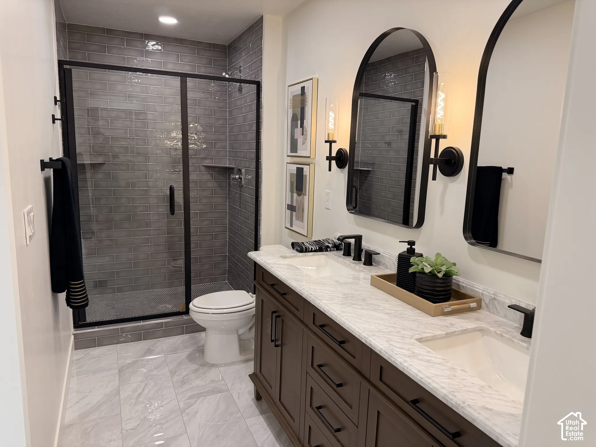 Double vanity with stone-look countertop, undermount sinks, matte black fixtures, arched wall mirrors, and a walk-in shower with grey tile surround