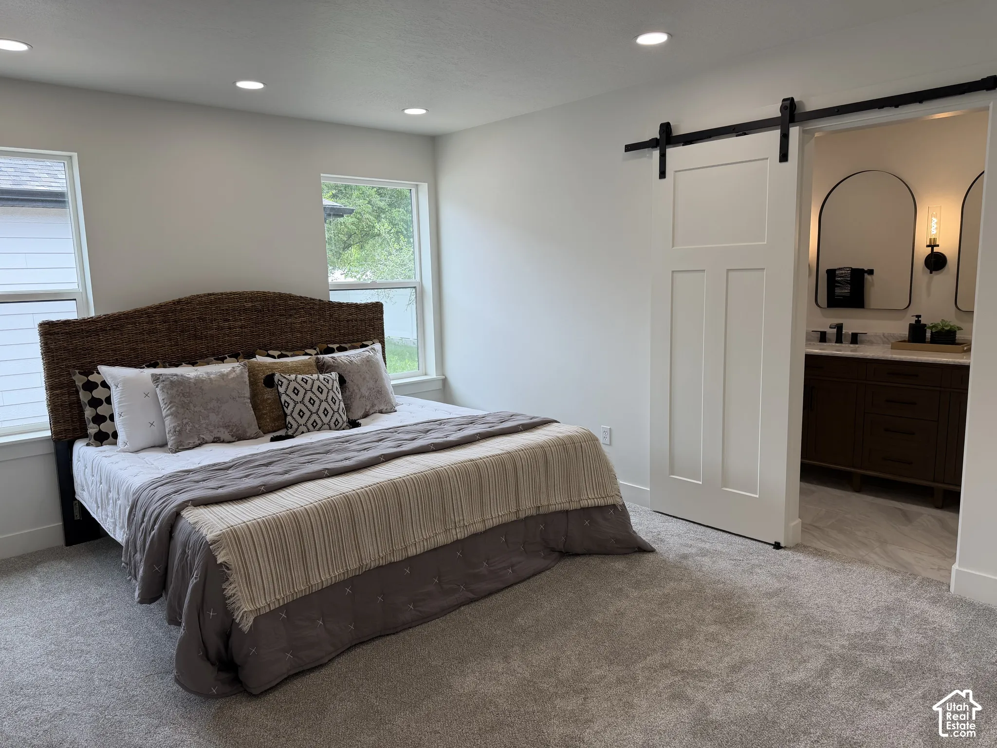 Neutral-toned bedroom featuring recessed lighting, plush carpeting, a white sliding barn-style door, and dual rectangular windows
