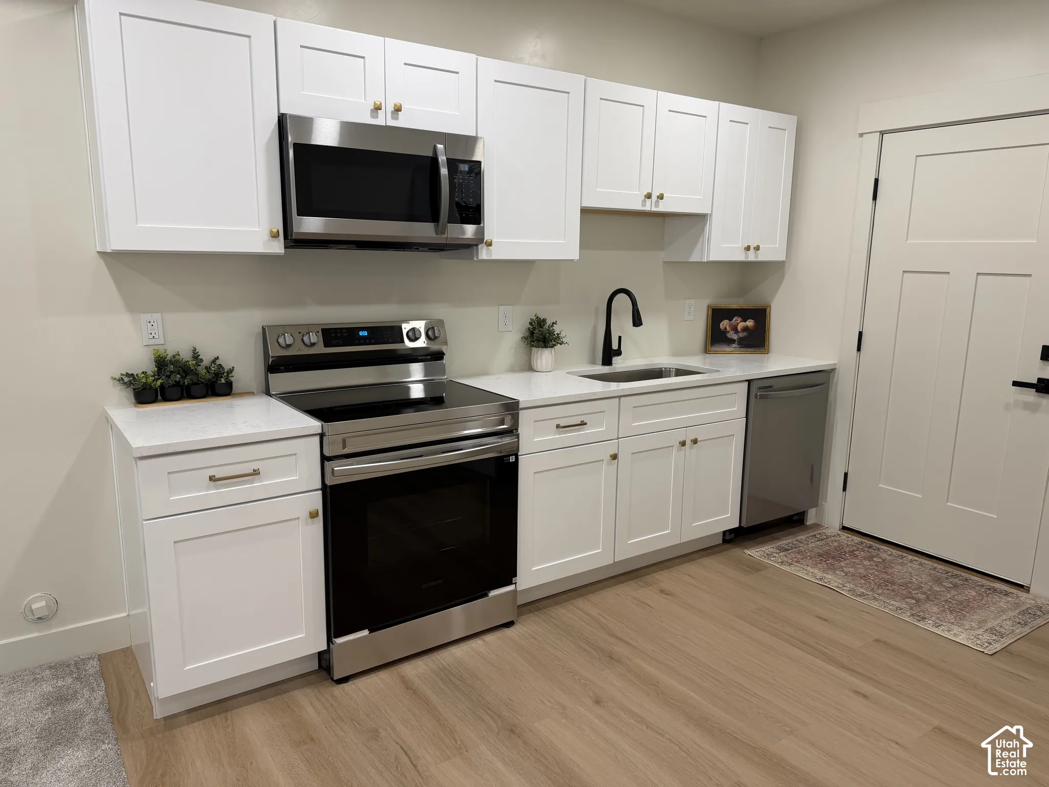 Kitchen featuring white Shaker-style cabinetry, stainless steel appliances, light-toned stone countertops, a matte black faucet, and wood-finish flooring