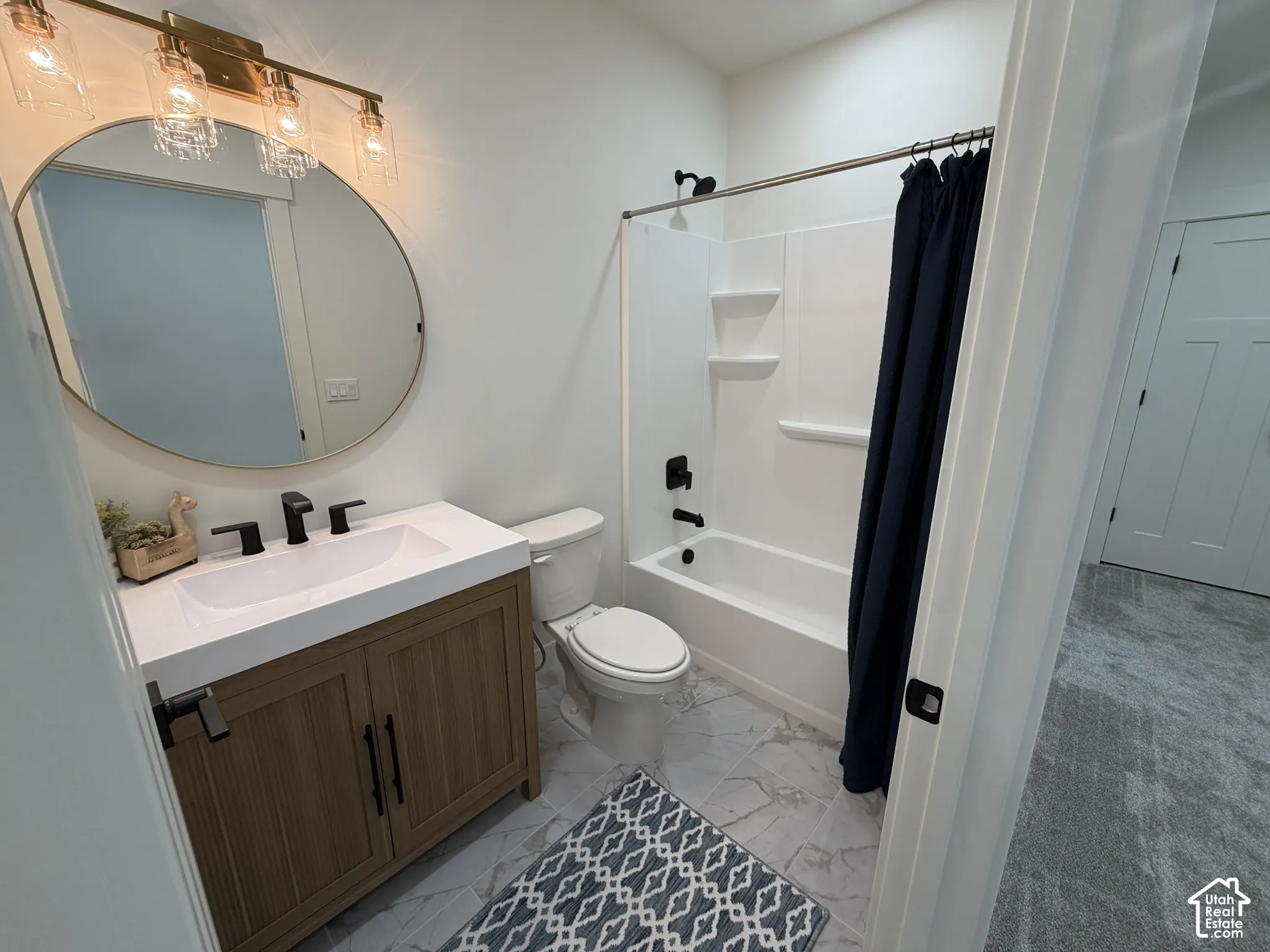 Bathroom featuring a wood-finish vanity with a rectangular sink, quartz countertop, matte black fixtures, round mirror, and a tub-shower combination with integrated shelving