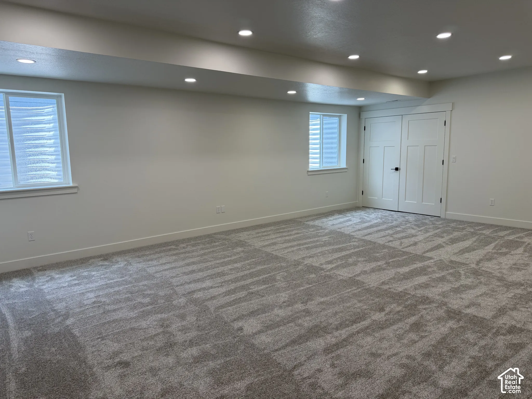 Open-concept space featuring recessed ceiling lighting, wall-to-wall carpeting, two egress-style windows, and double interior doors with matte black hardware