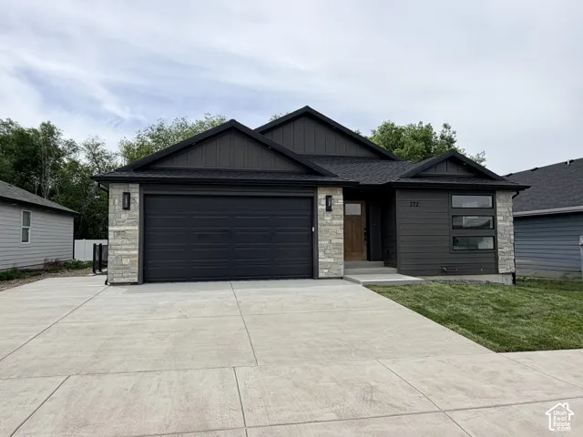 Modern exterior featuring horizontal lap siding, stacked stone masonry, a dark metal-accented garage door, and a natural wood entry door with glass paneling