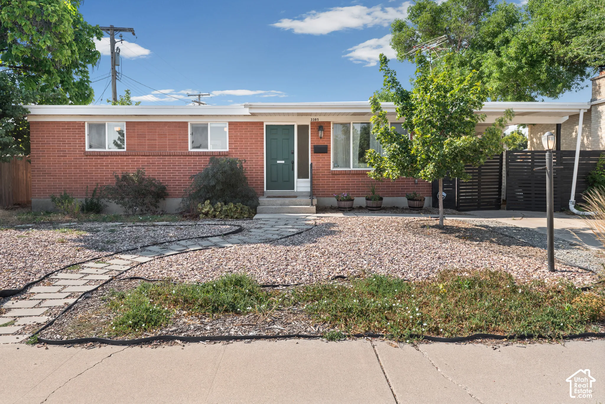 Single-story red brick exterior featuring a covered carport, stone paver walkway, and low-maintenance rock landscaping