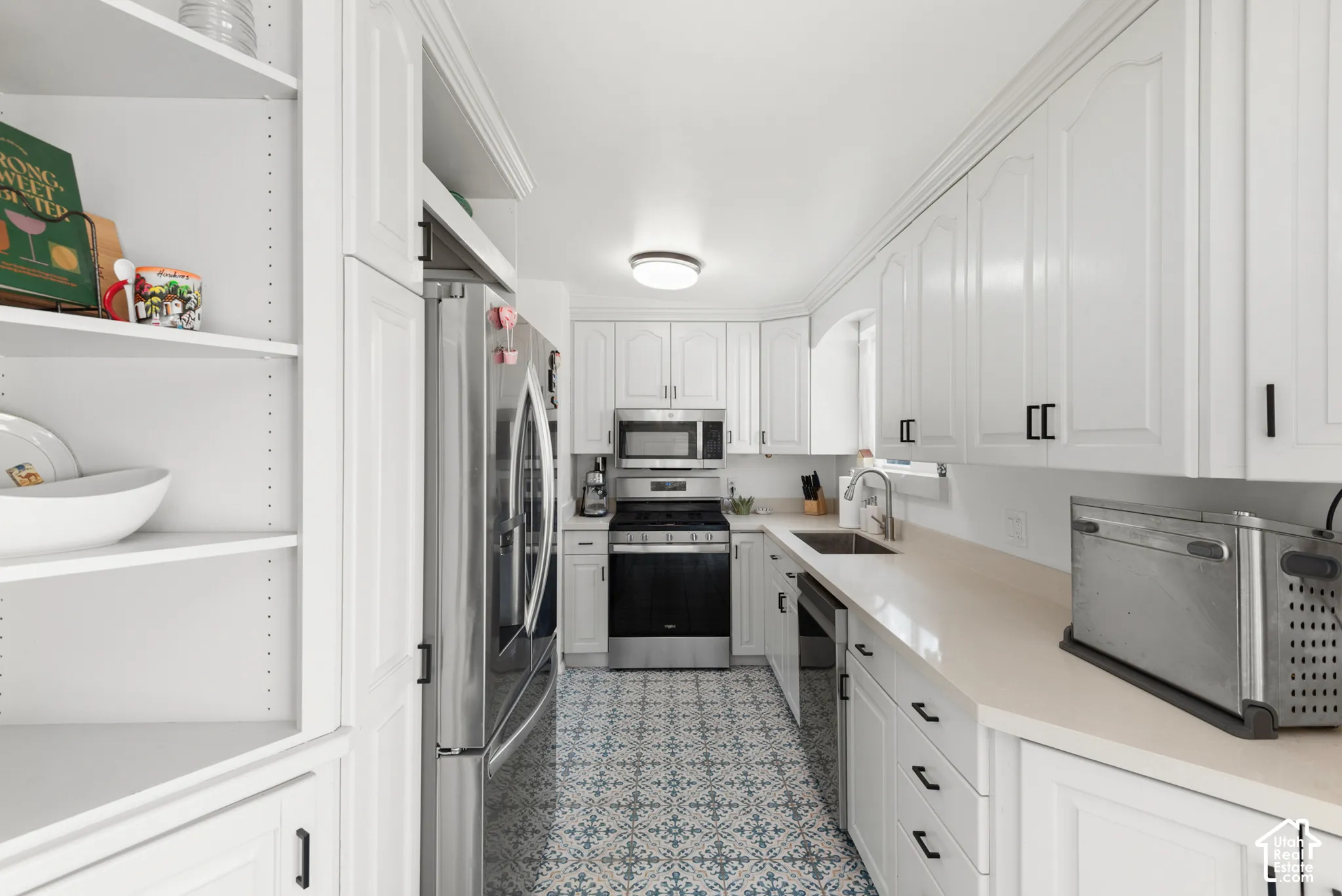 Kitchen featuring white cabinetry, solid-surface countertops, stainless steel appliances, decorative tile flooring, and integrated open shelving