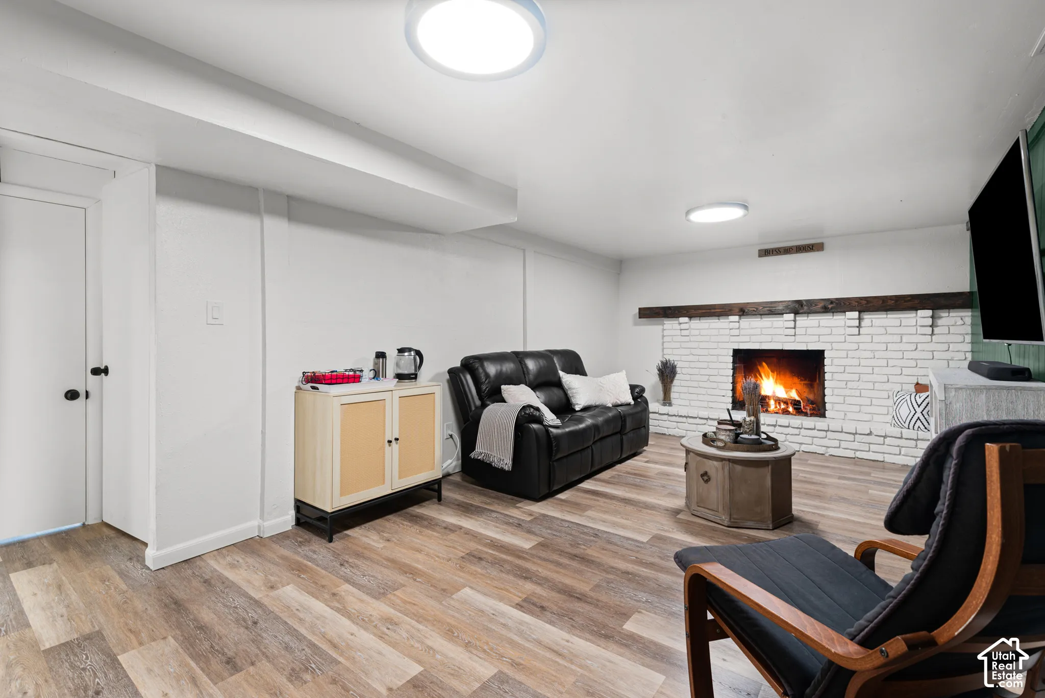 White-painted brick fireplace with a dark wood mantel and wood-finish flooring