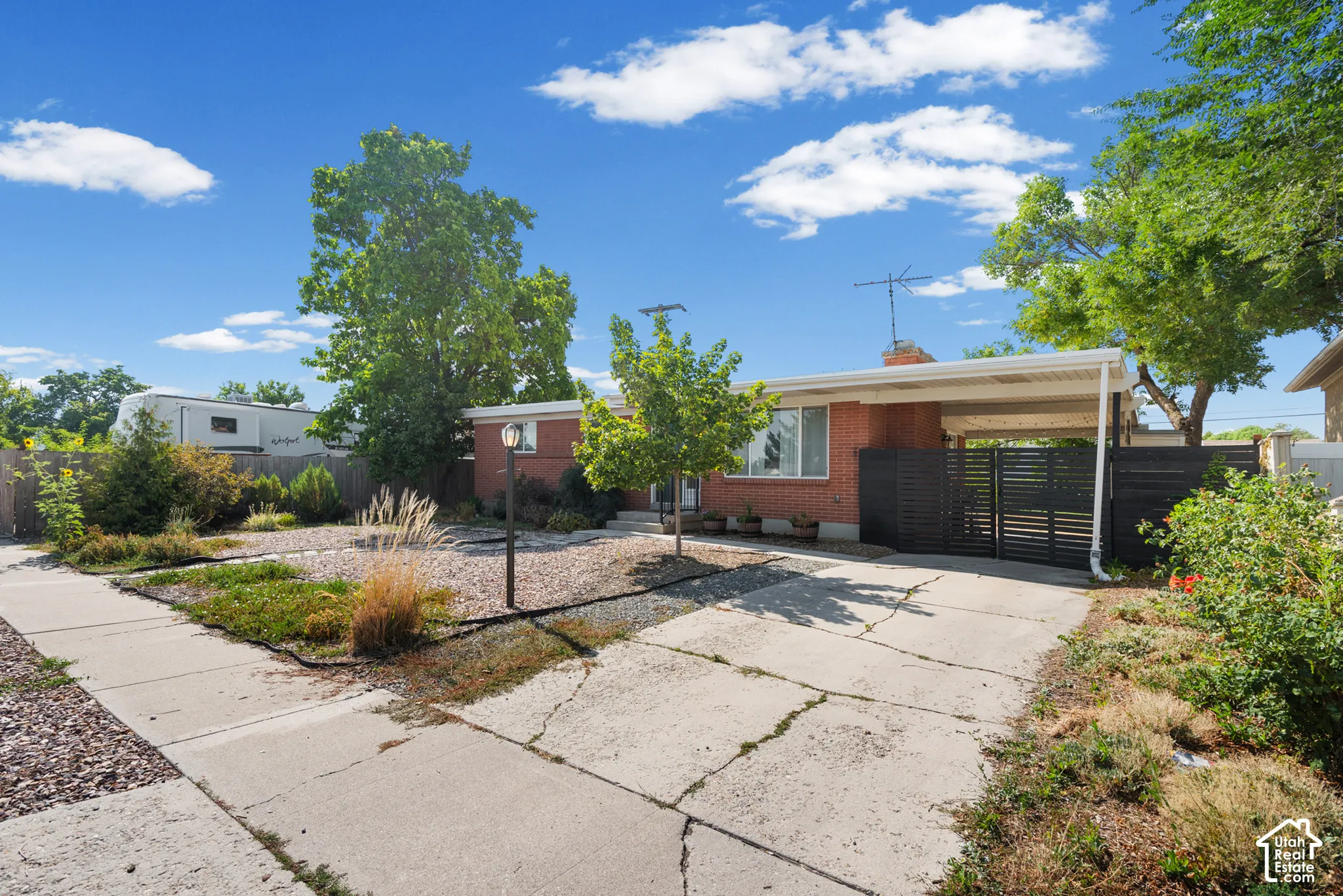 Red brick exterior featuring a covered carport, horizontal slat privacy fencing, concrete driveway, and xeriscaped front yard