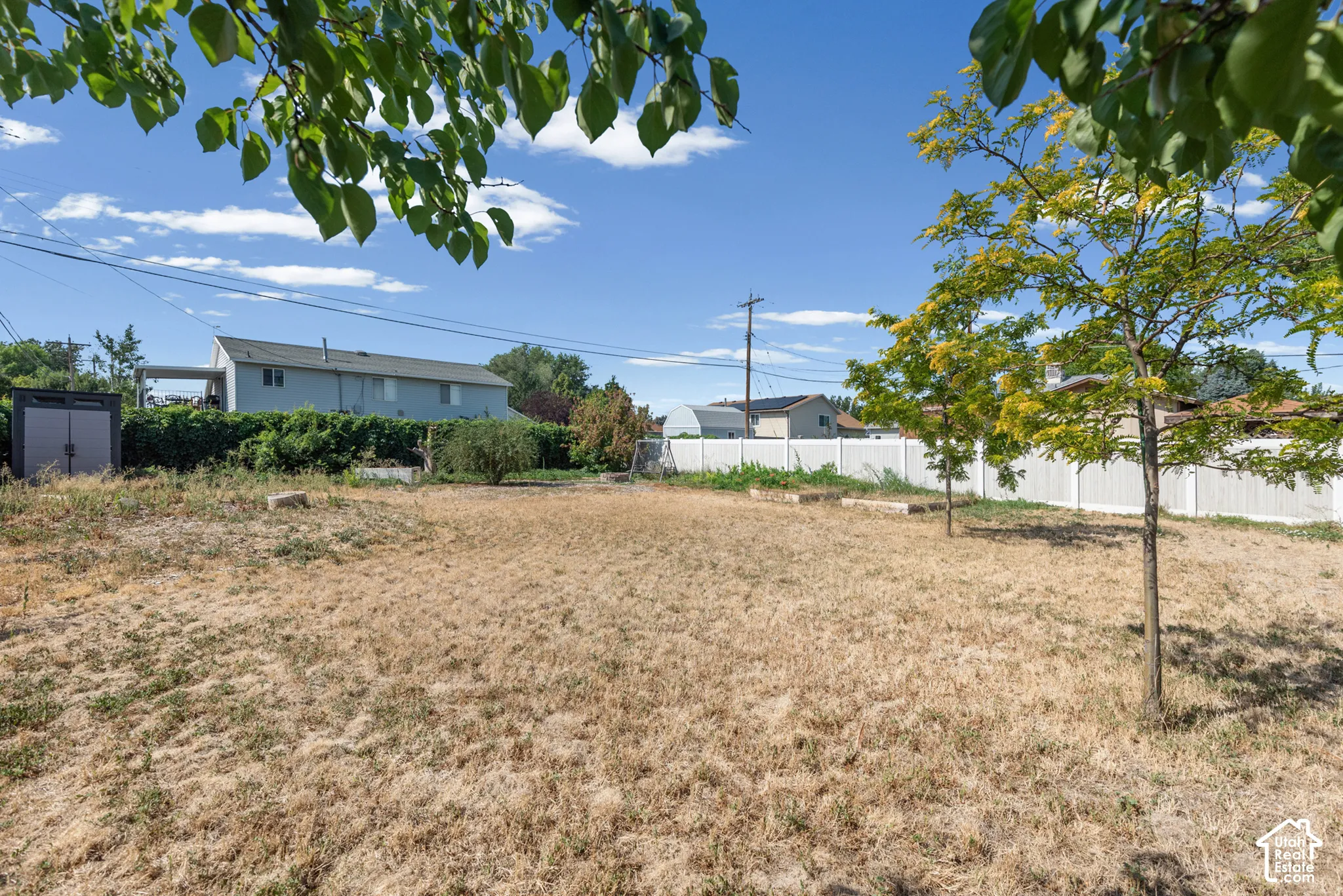Expansive backyard featuring mature trees, vinyl fencing, and a detached storage structure