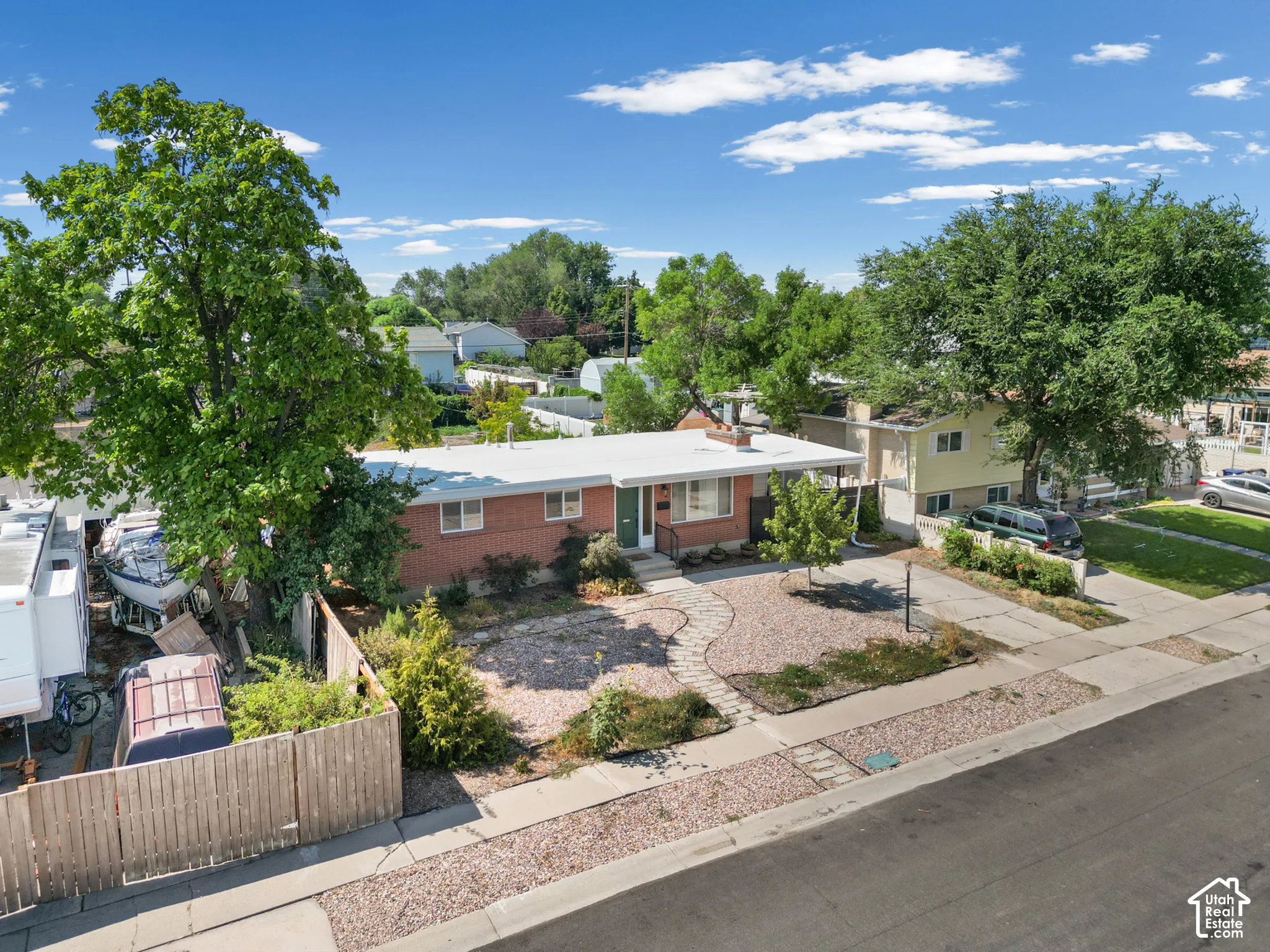 Single-level brick exterior featuring a flat roofline, stone walkway, mature trees, and detached wood fencing