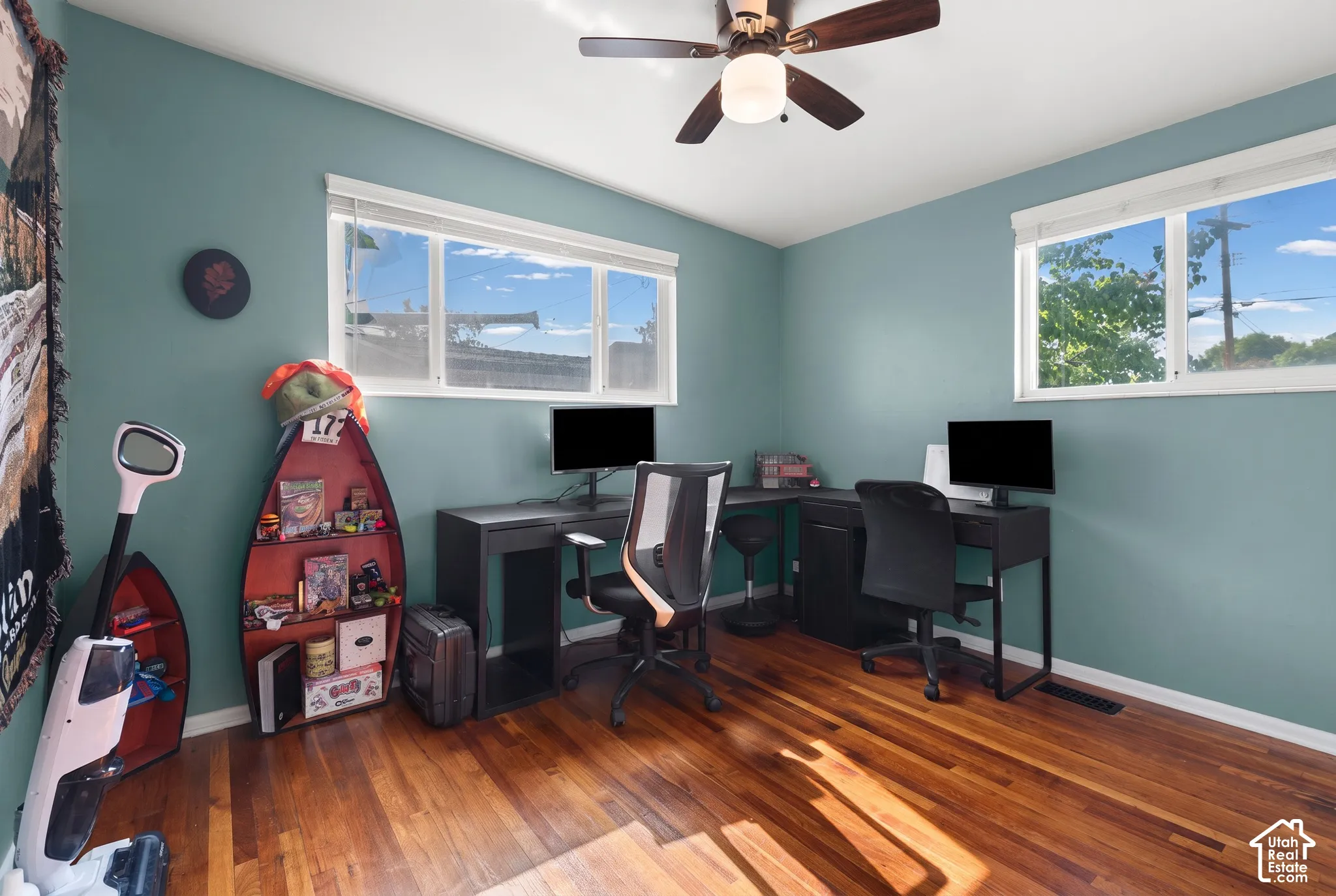 Room featuring wood-finish flooring, dual windows, and a ceiling-mounted light fixture with a fan