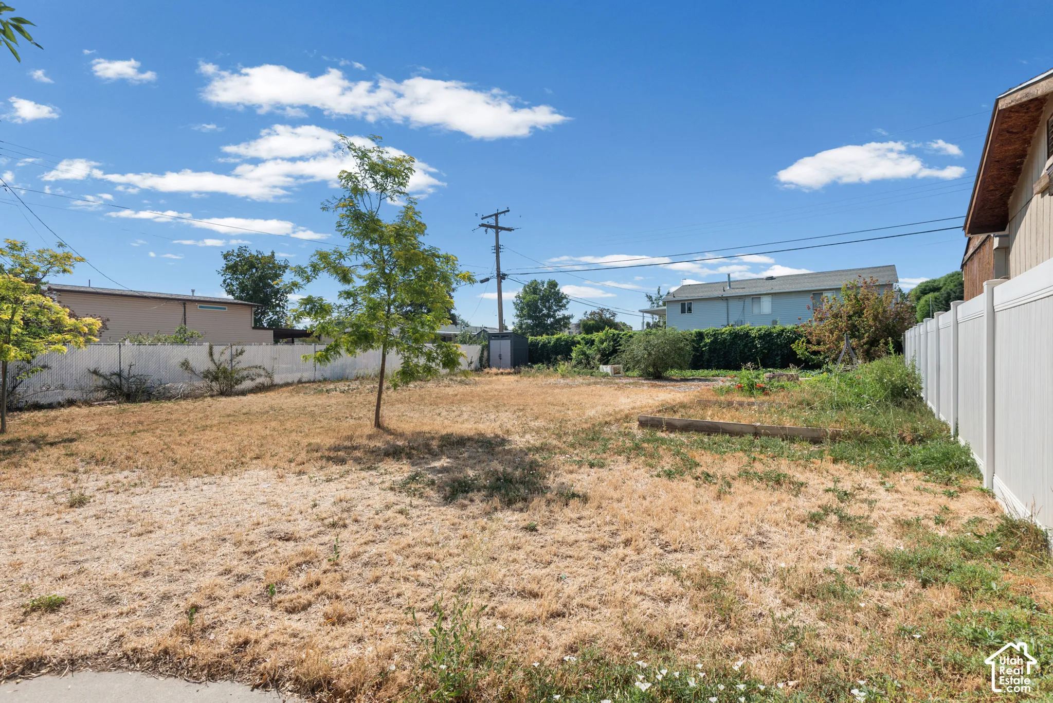 Expansive backyard featuring a white vinyl privacy fence, mature trees, and a detached storage structure