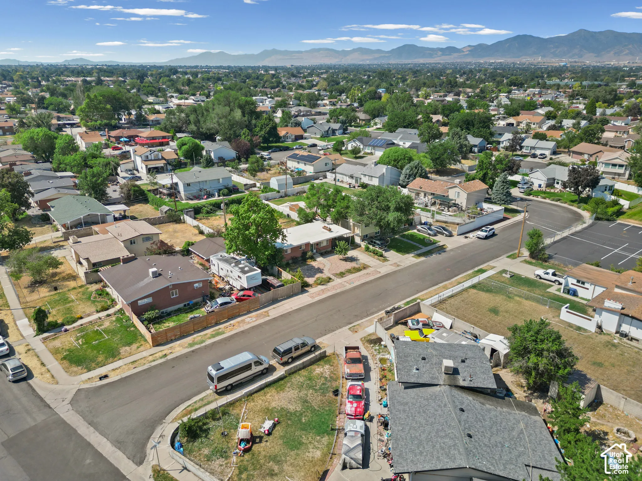 Aerial perspective of the residential area featuring asphalt street infrastructure, mature trees, and a mountain range backdrop