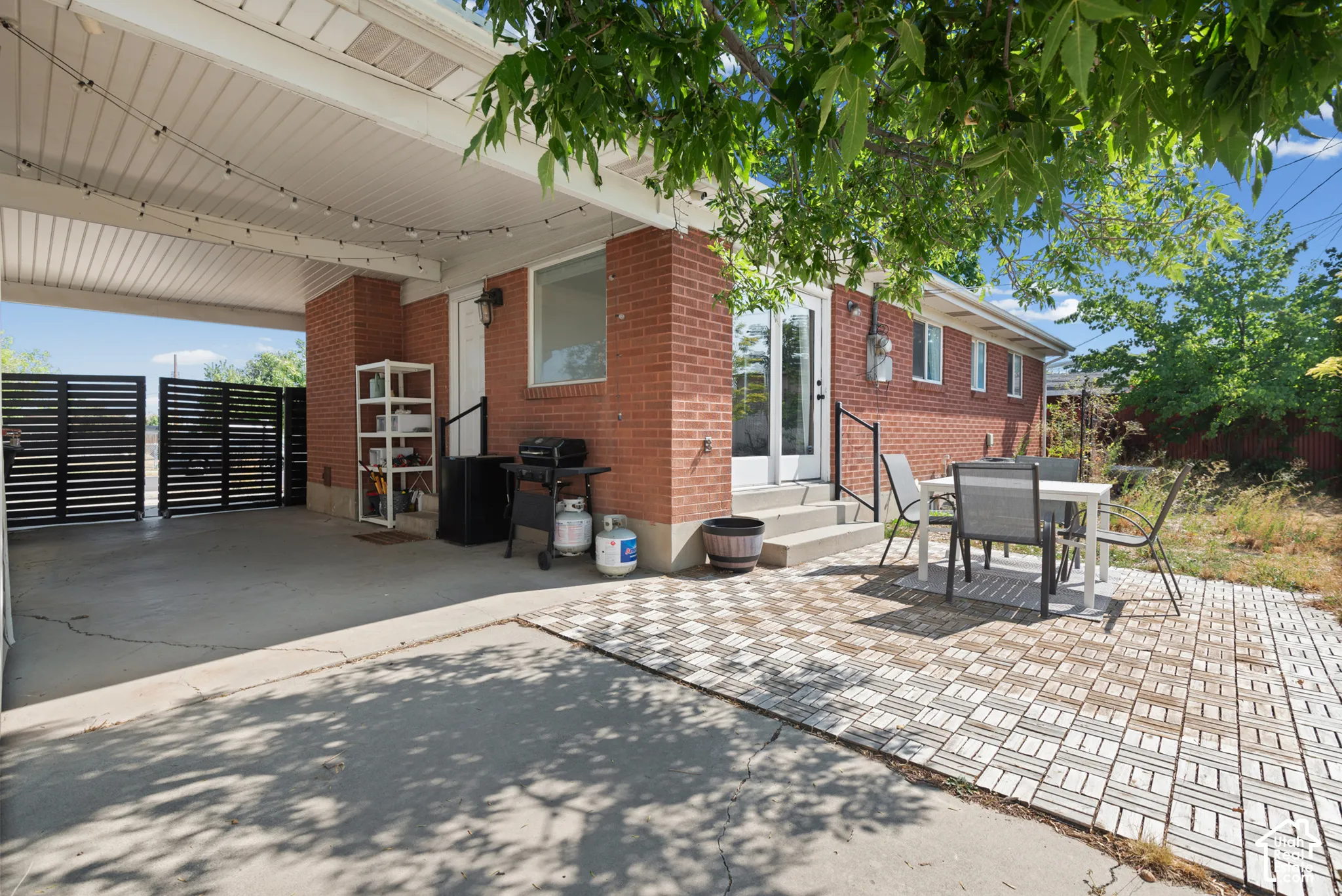 Exterior red brick facade featuring a covered carport, concrete and paver patio, and horizontal privacy fencing