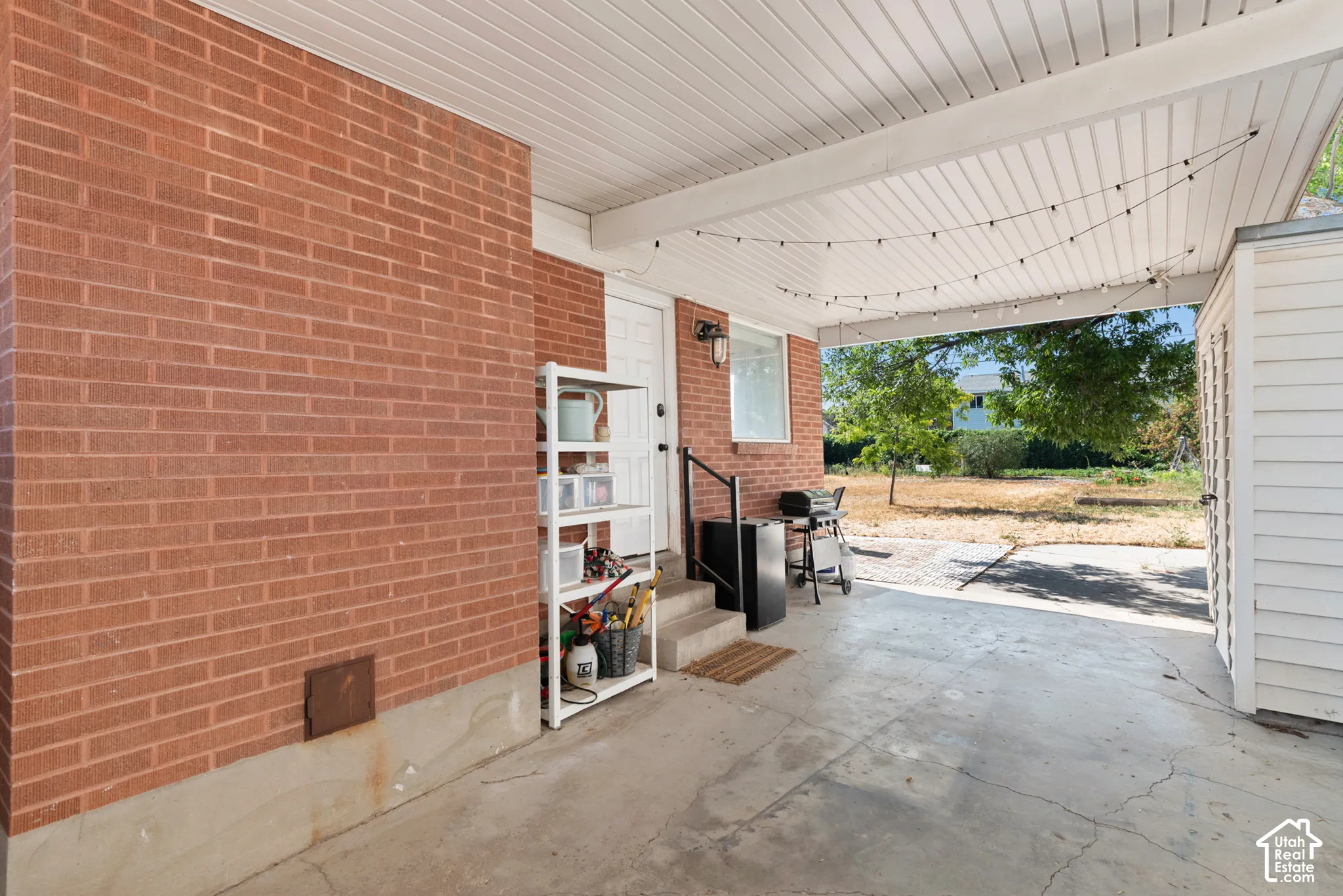 Covered exterior patio featuring red brick masonry, concrete flooring, and horizontal siding