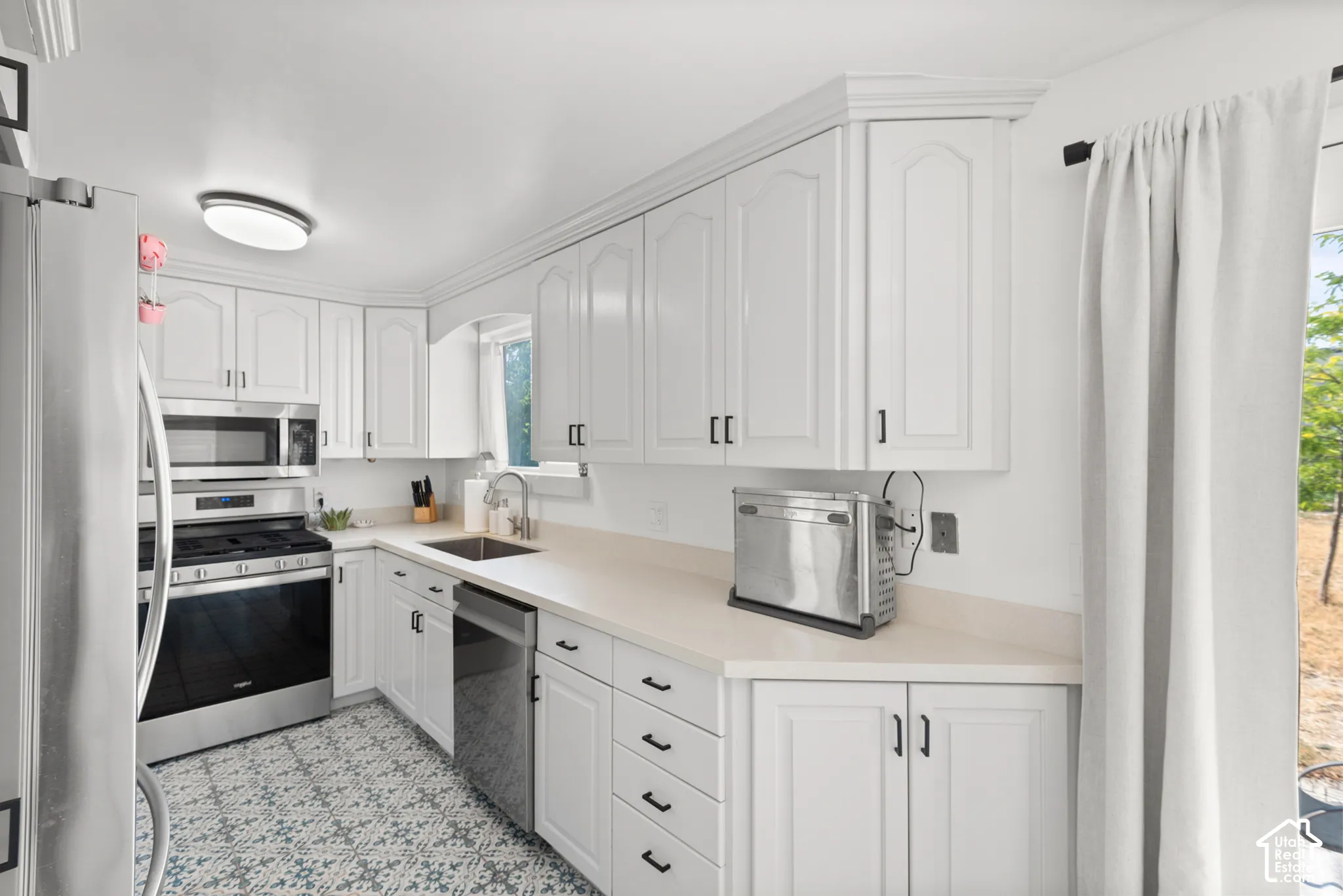 Kitchen featuring white cabinetry with matte black hardware, solid surface countertops, stainless steel appliances, and patterned tile flooring