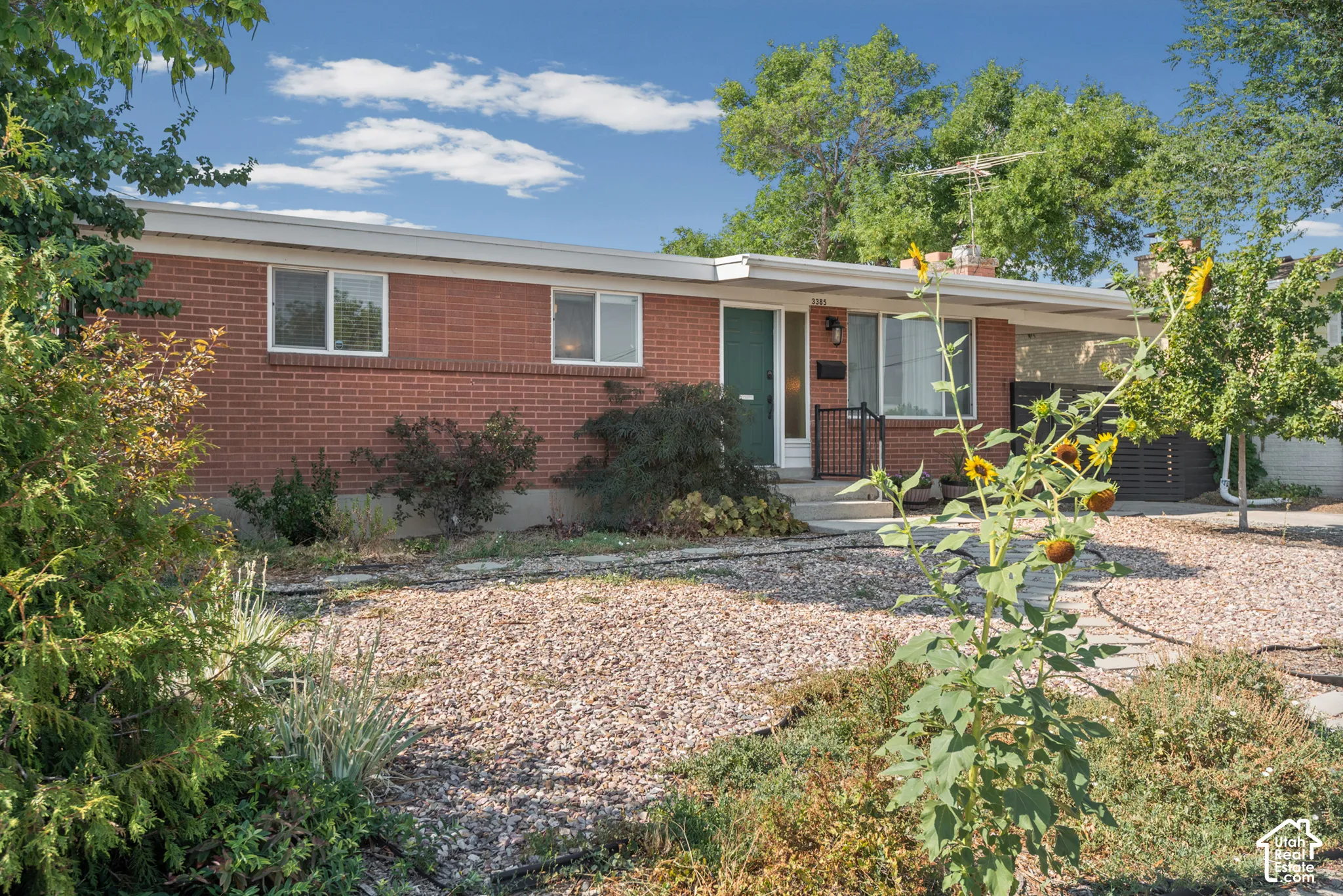 Single-story brick exterior featuring a low-slope roof, covered carport, and xeriscaped front yard