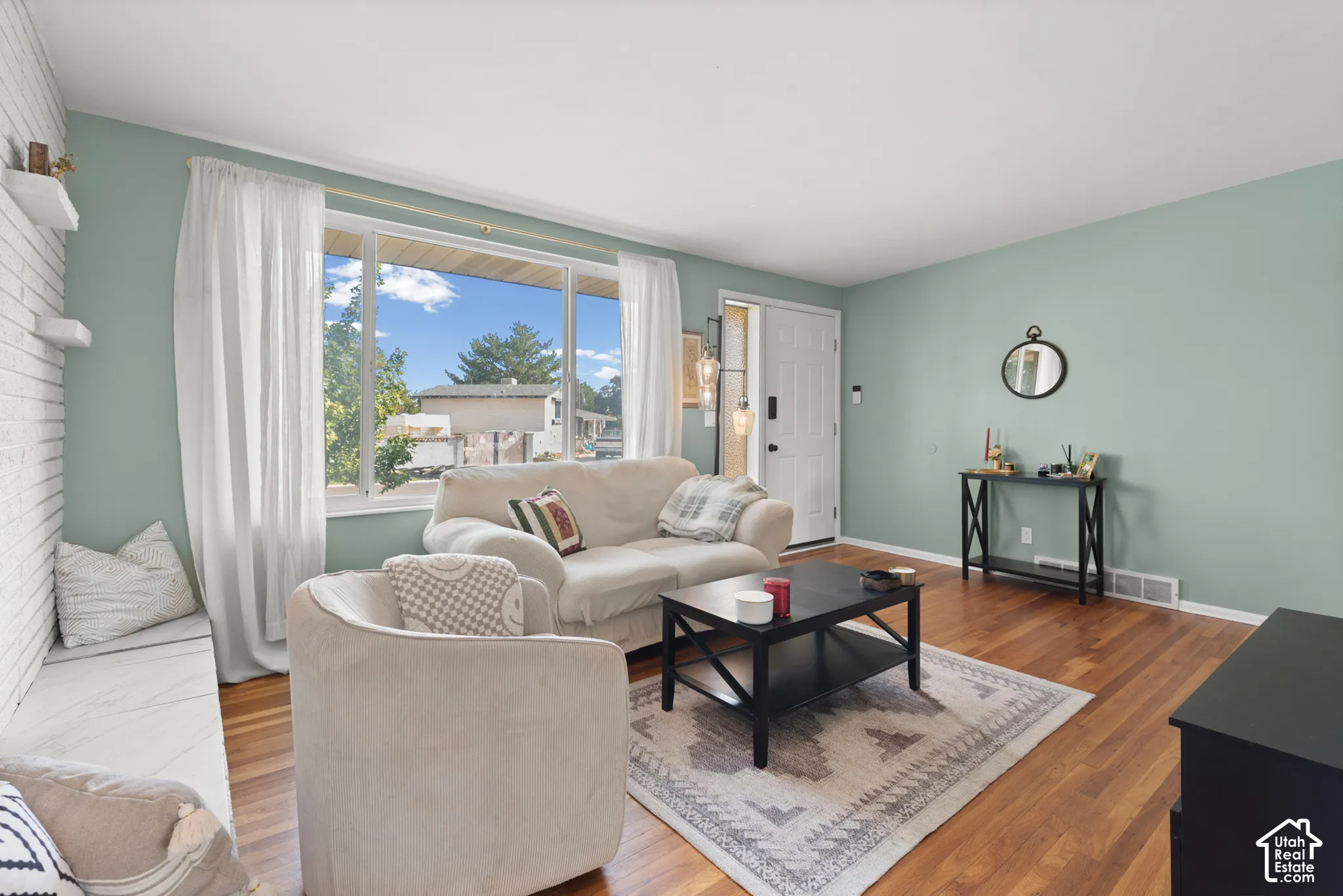 Living area featuring wood-finish flooring, a painted brick fireplace surround with built-in bench seating, and a large picture window