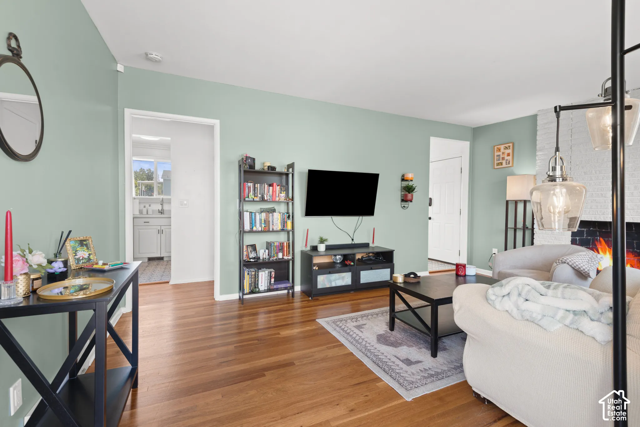 Living area featuring wood-finish flooring, a white-painted brick fireplace with a black surround, and glass pendant lighting