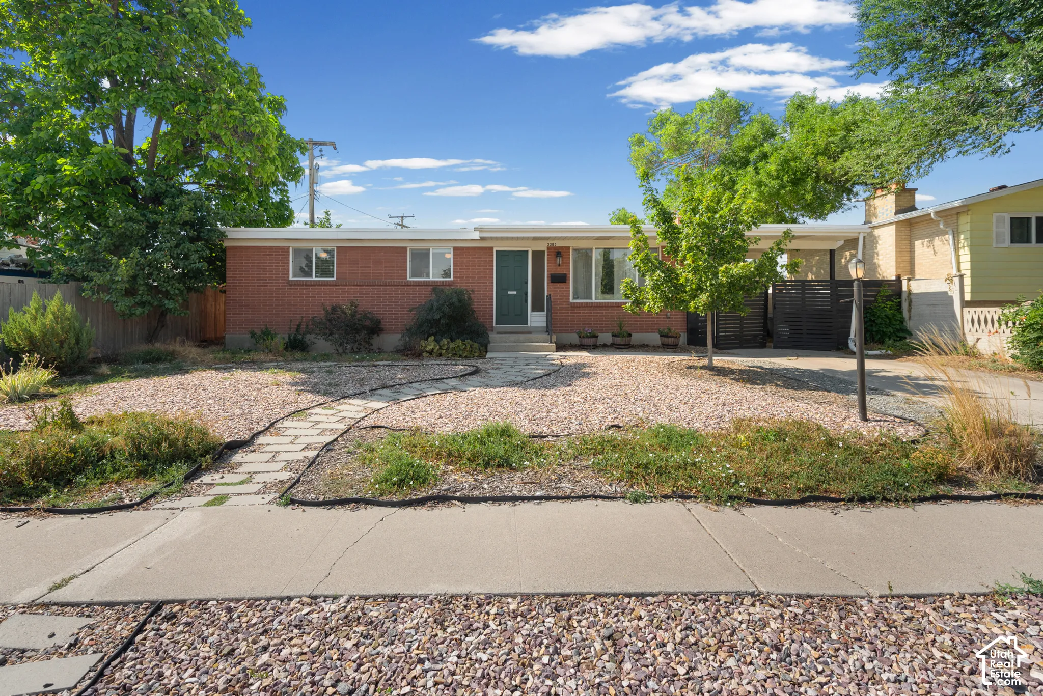 Mid-century red brick exterior featuring a flat roofline, stone-paver walkway, gravel landscaping, and a covered carport area