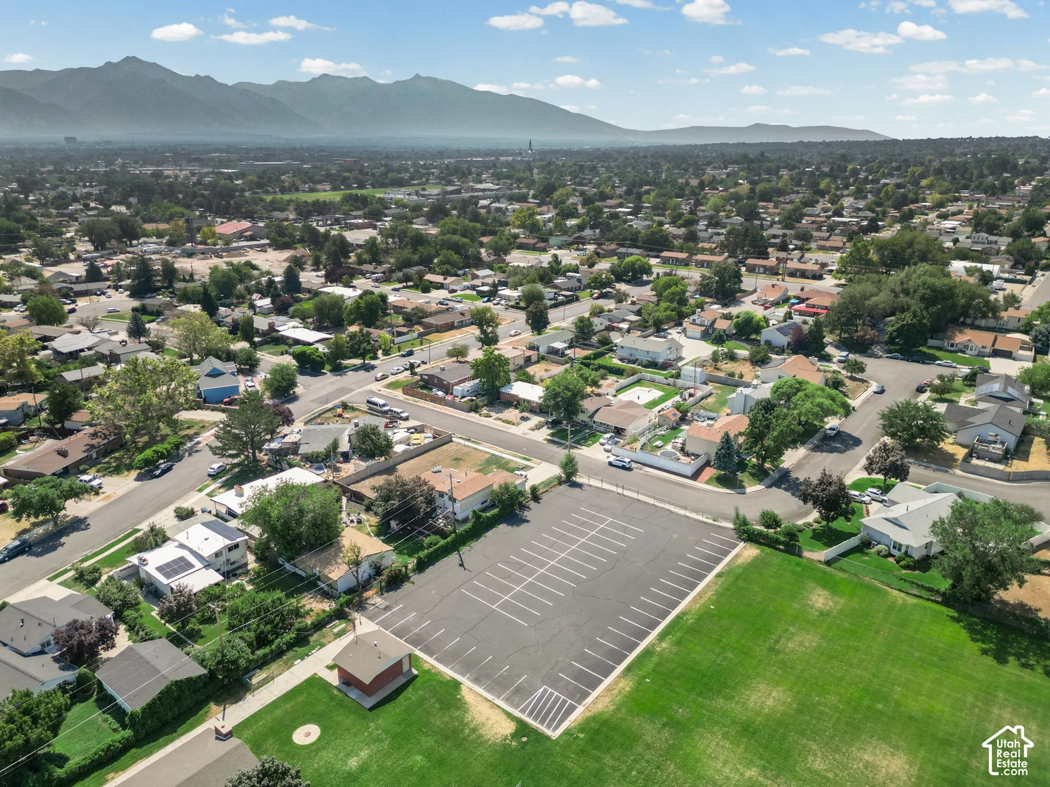 Aerial perspective featuring an expansive lawn, paved parking lot, and mountain range backdrop