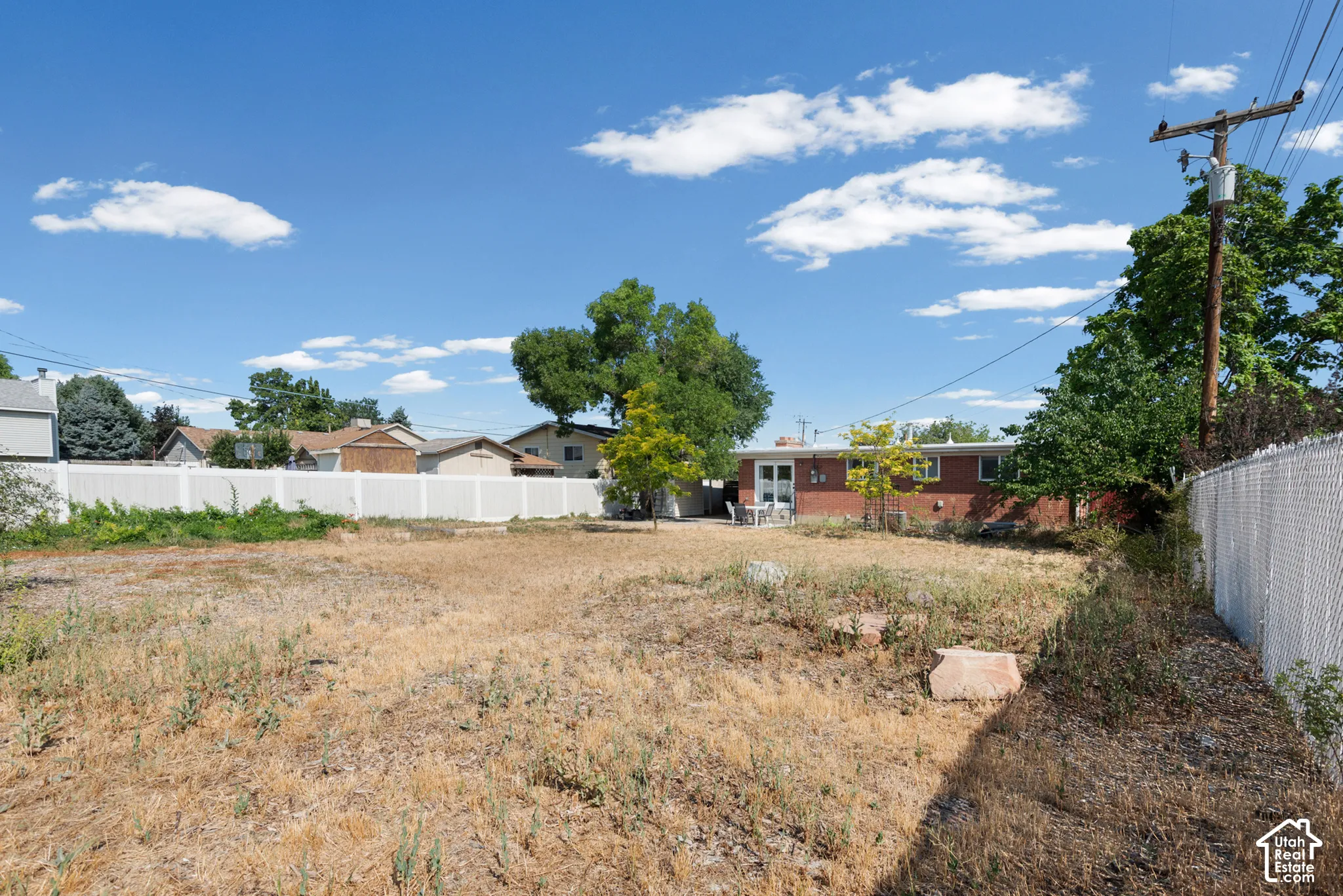 Expansive backyard featuring a solid-surface perimeter fence, masonry exterior wall, mature trees, and natural landscaping