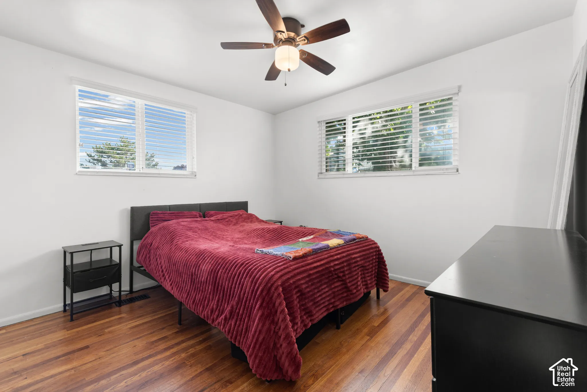 Room featuring wood-finish flooring, dual windows with blinds, and a ceiling-mounted light fixture with a fan
