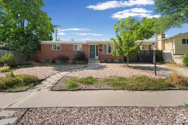 Mid-century red brick exterior featuring a flat roofline, stone-paver walkway, gravel landscaping, and a covered carport area