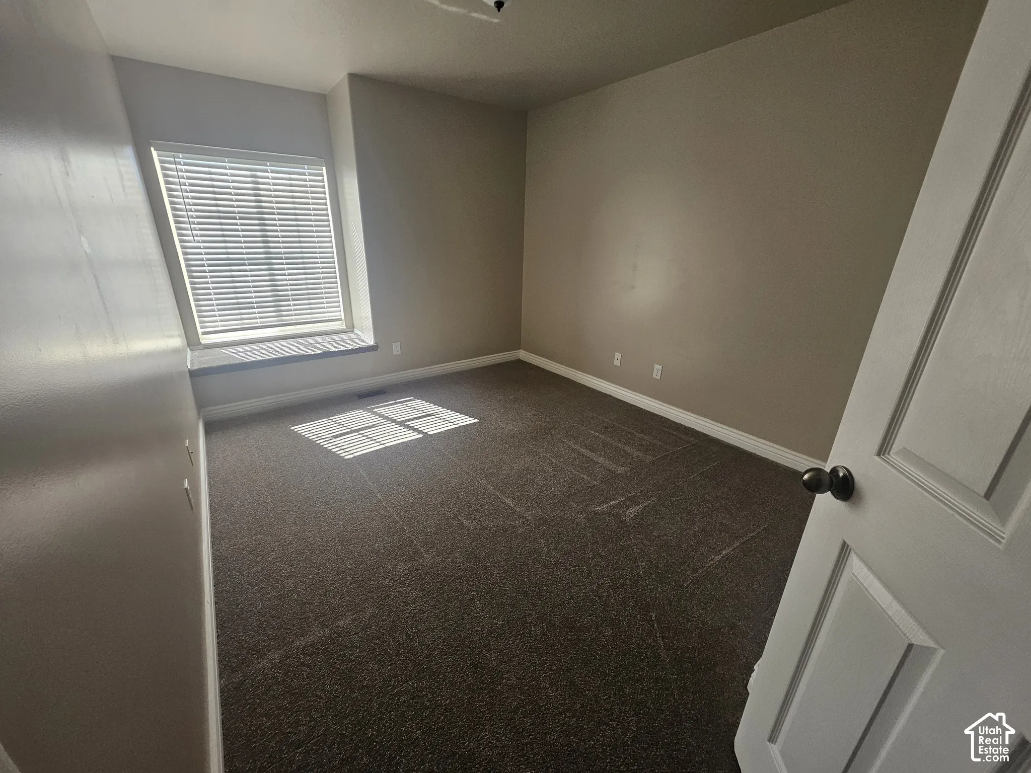 Room featuring neutral wall tones, carpeted flooring, a recessed window nook, and a multi-panel interior door with dark hardware