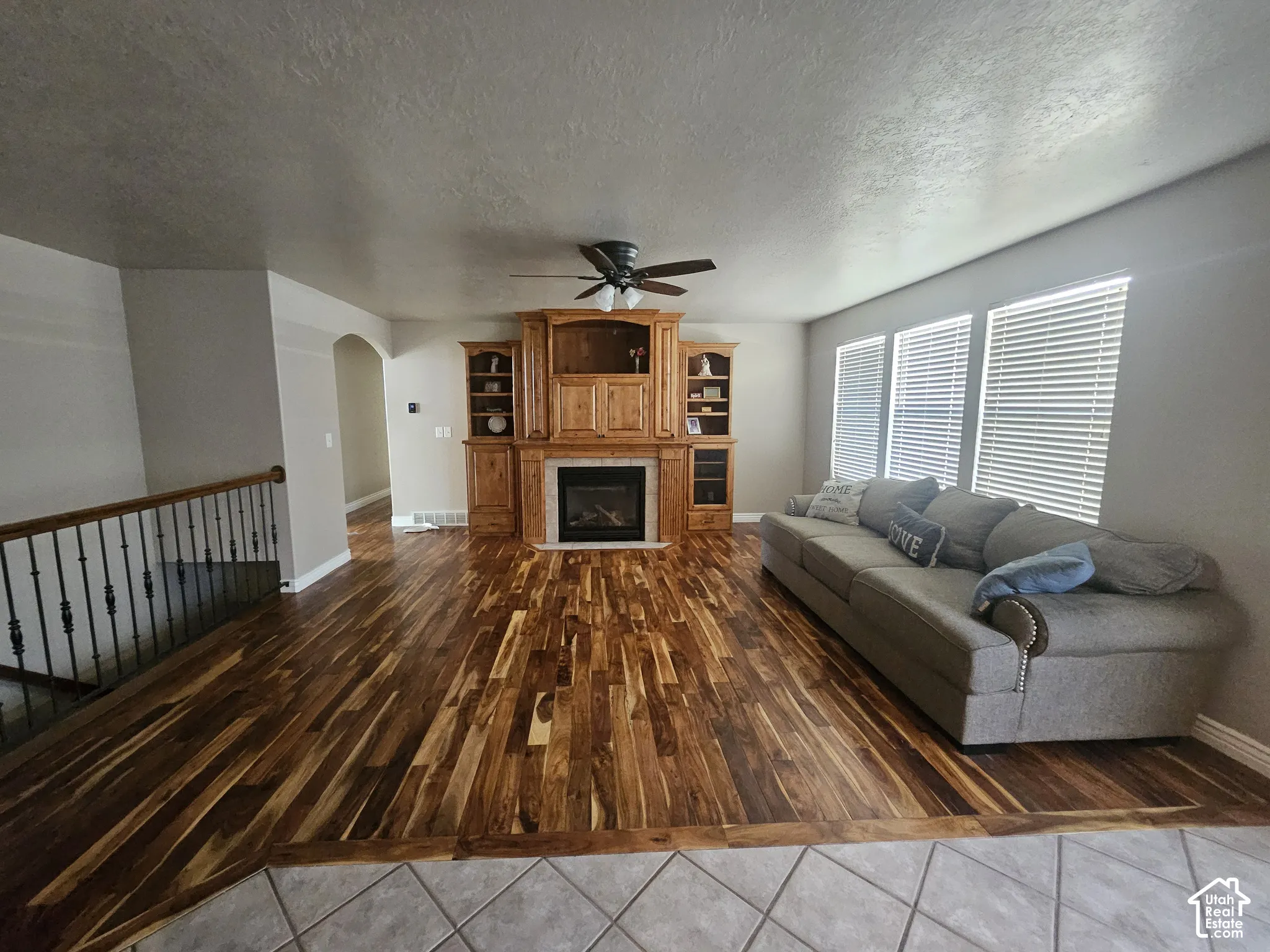 Living area featuring wood-finish flooring, a floor-to-ceiling built-in wood cabinetry unit, an integrated fireplace, and a metal spindle railing