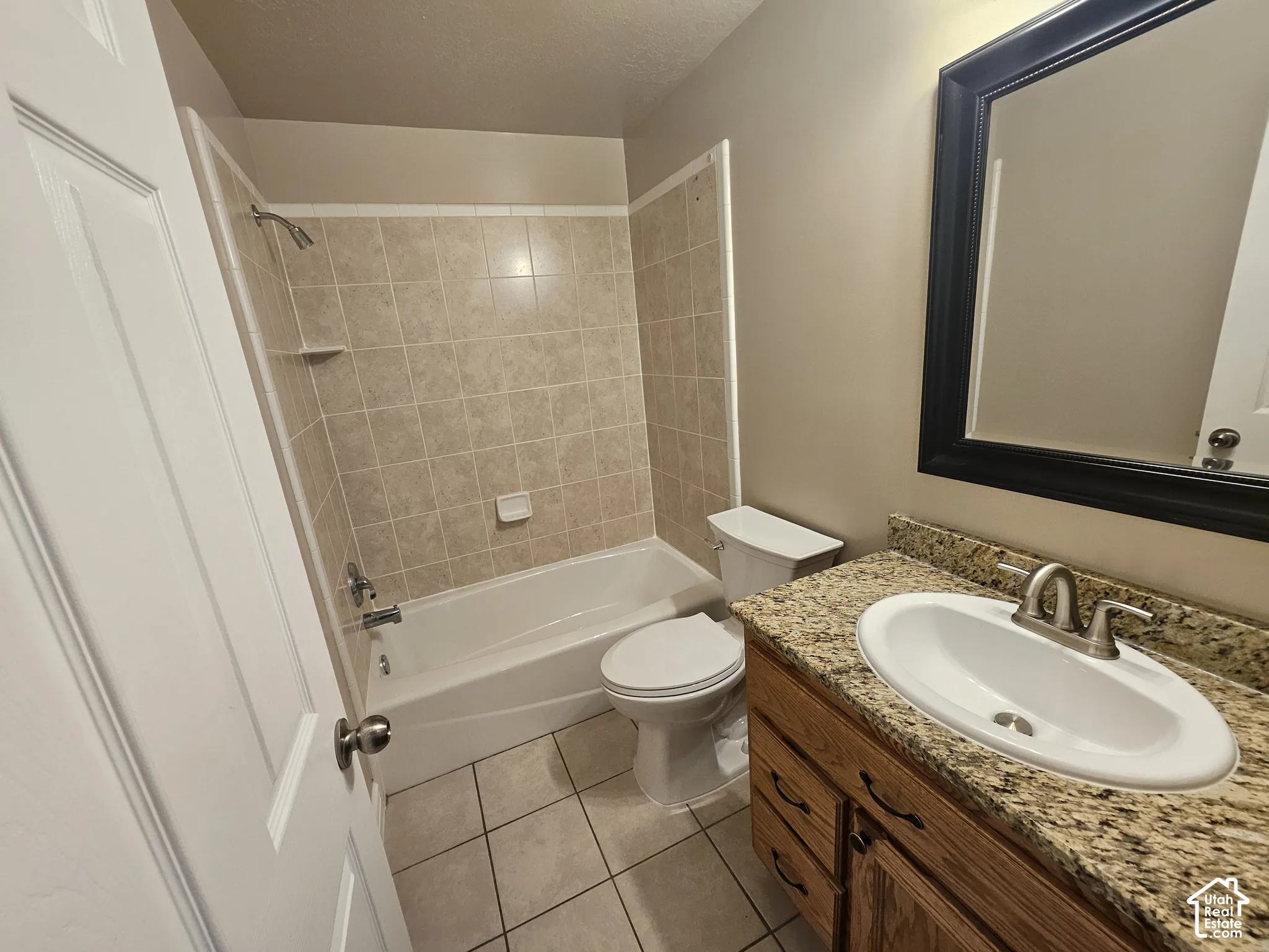 Bathroom featuring a stone-look countertop, integrated vanity cabinetry, ceramic tile shower surround, and tile flooring