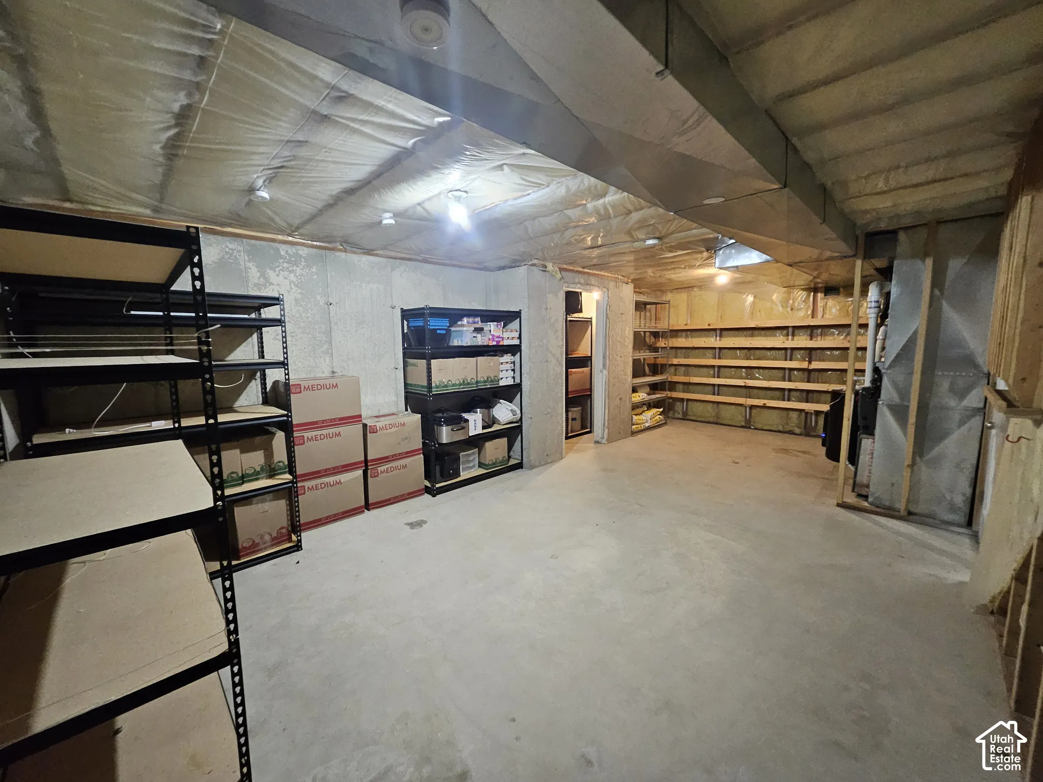 Storage room featuring concrete flooring, foundation walls, open wood shelving, and exposed insulation