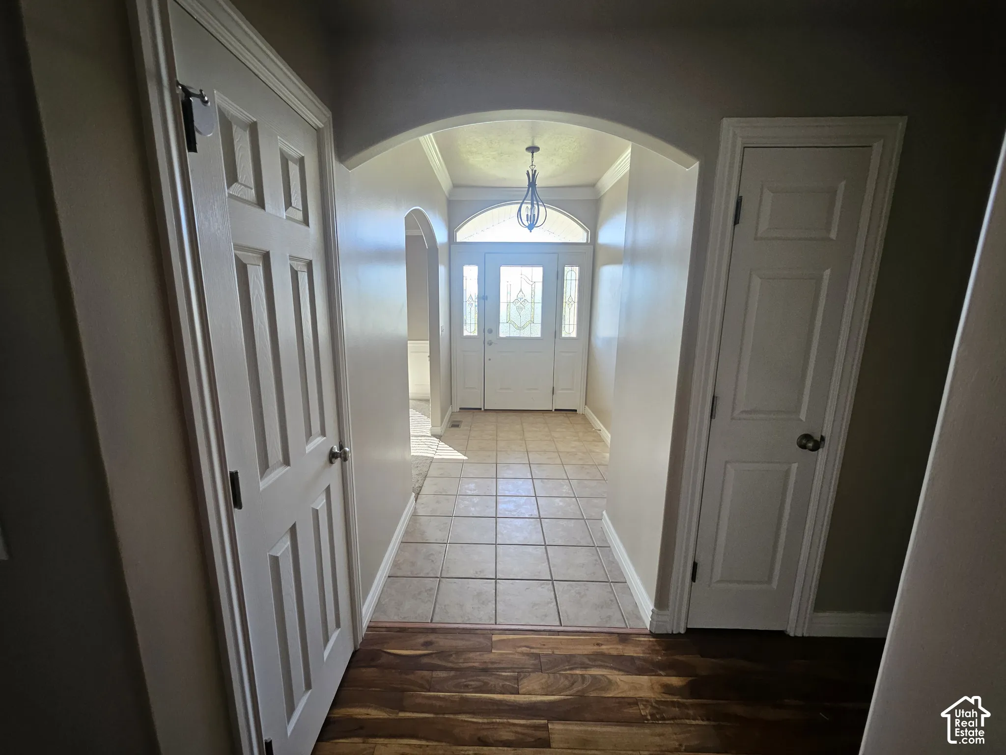 Entryway featuring an arched opening, tile flooring, wood-finish flooring, a multi-panel door with a glass inlay and transom window, and a hanging light fixture