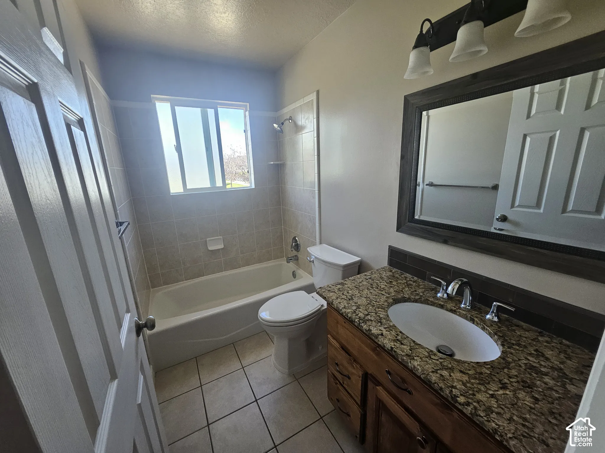 Bathroom featuring a stone-surface vanity with an integrated basin, wood-finish cabinetry, tile-surround tub, and tiled flooring