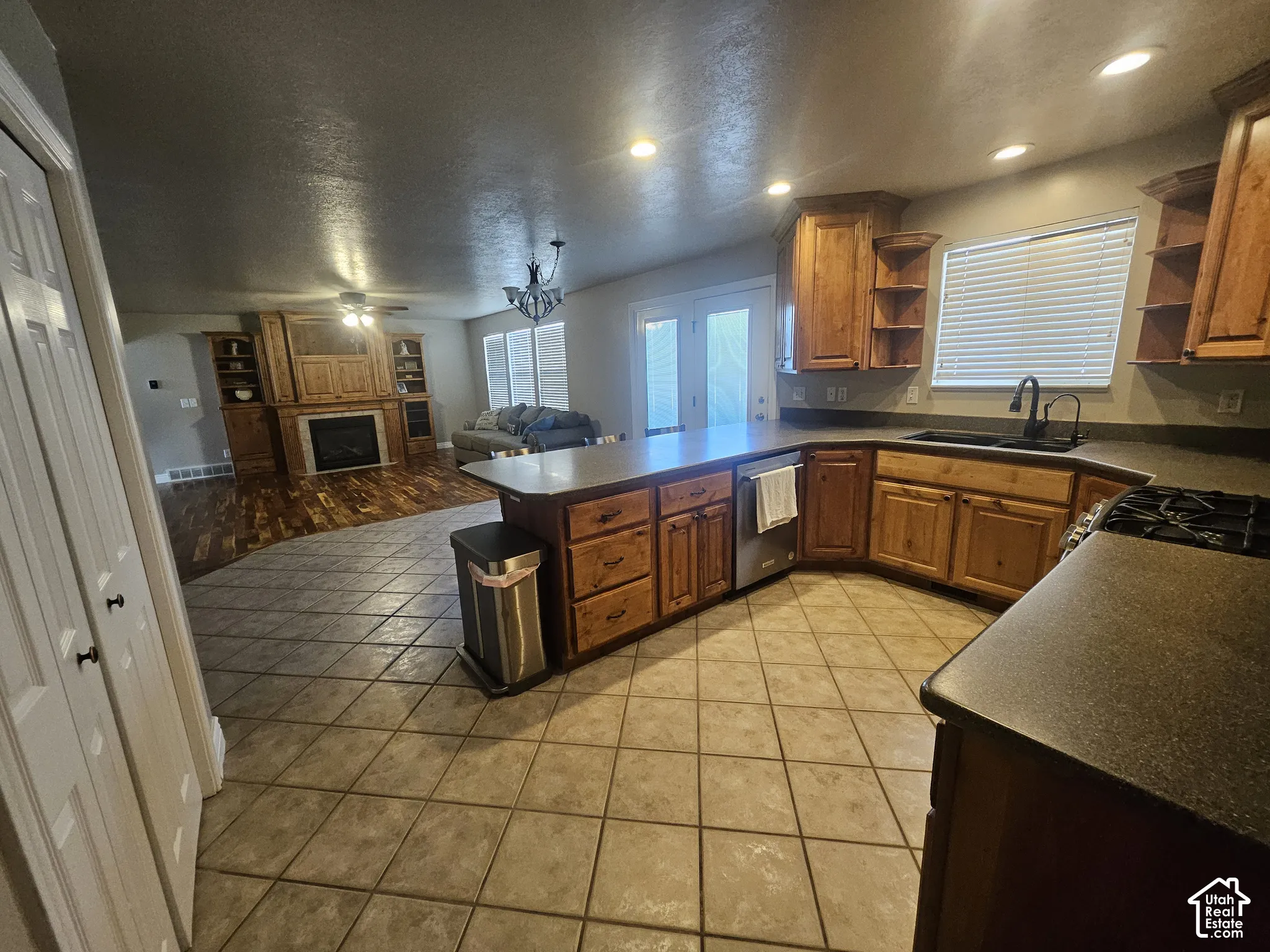 Kitchen featuring custom wood cabinetry, dark countertops, tile flooring, and recessed lighting, with a fireplace and wood-finish flooring visible in the background