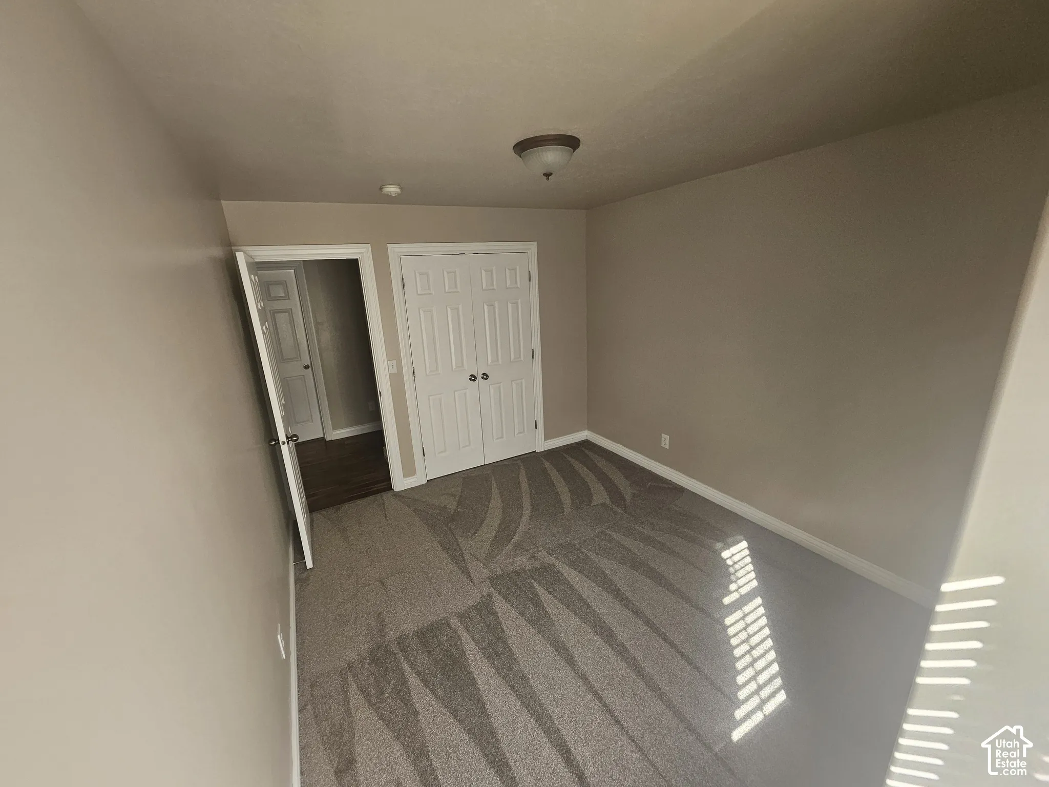Interior room featuring neutral wall paint, wall-to-wall carpeting, dual-panel closet doors, and a flush-mount ceiling light fixture