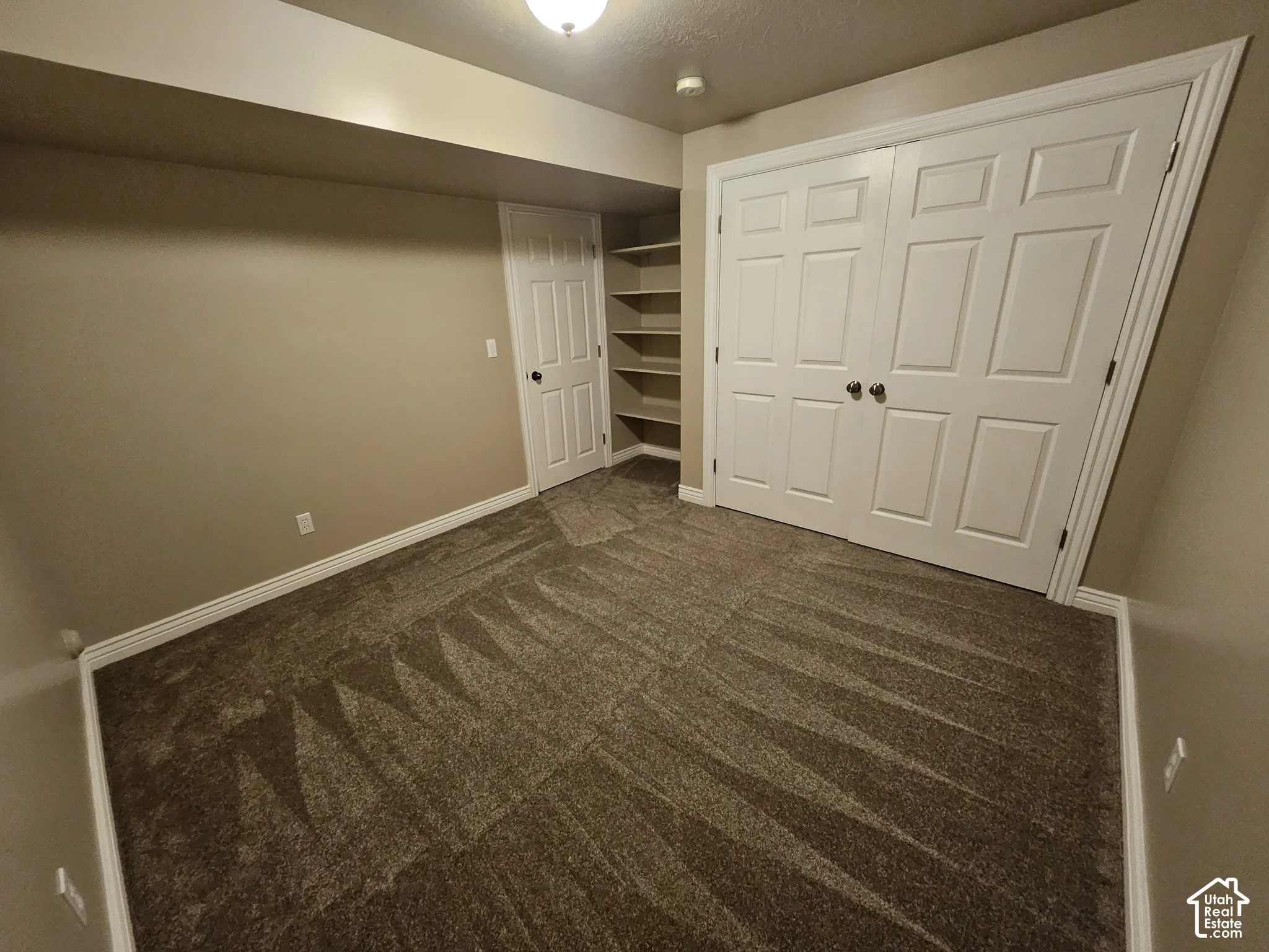 Neutral-toned room featuring wall-to-wall carpeting, double-door closet, single-door entry, and built-in wall shelving