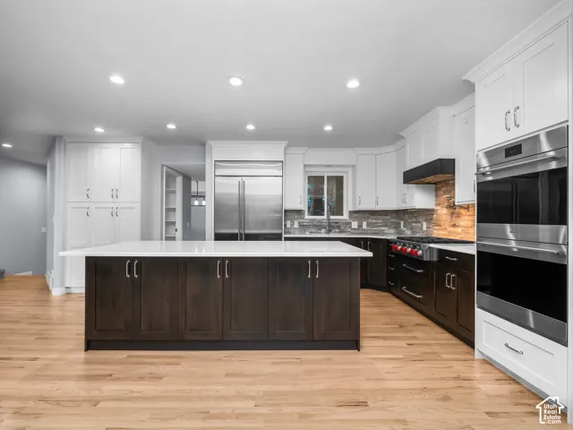 Kitchen featuring a central island with white quartz countertop, dual-tone custom cabinetry, stainless steel appliances, and wood-finish flooring