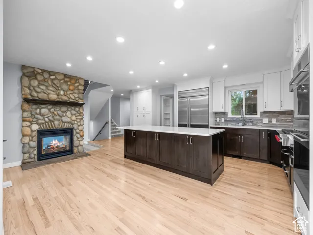 Natural river rock fireplace, wood-finish flooring, center island with stone countertop, stainless steel refrigerator, and recessed lighting