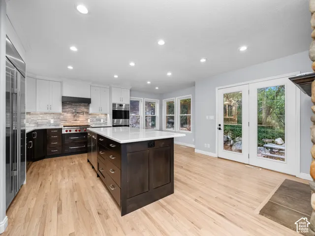 Kitchen featuring a central island with white stone countertop, dual-tone cabinetry, stainless steel professional-grade appliances, wood-finish flooring, and glass-paneled double doors