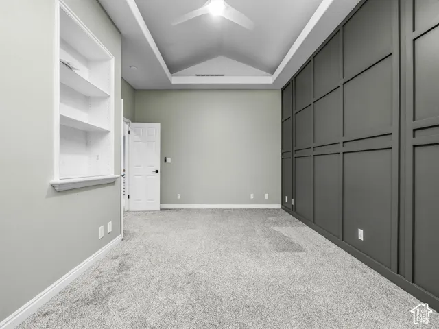Vaulted ceiling featuring a central recessed detail, wall-to-wall carpeting, charcoal-colored grid-patterned wainscoting, and a recessed built-in shelving unit