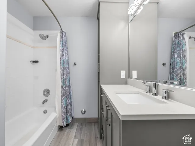 Bathroom featuring a vanity with integrated cabinetry, solid surface countertop, wood-finish flooring, and a tub-shower combination with tiled surround